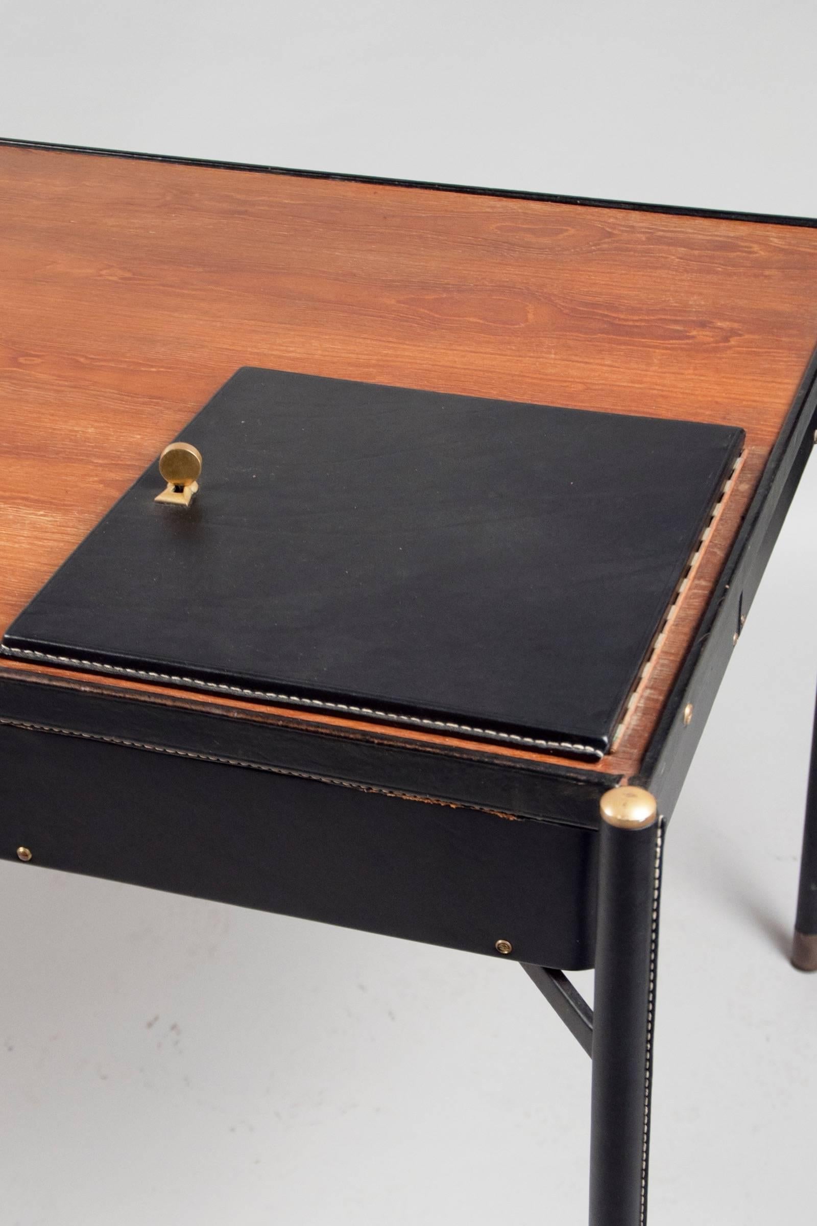 Tubular metal desk covered in black saddle-stitched leather; with an oak work surface containing a lockable leather door, revealing a pivoting compartment underneath.

OUR REFERENCE N9917