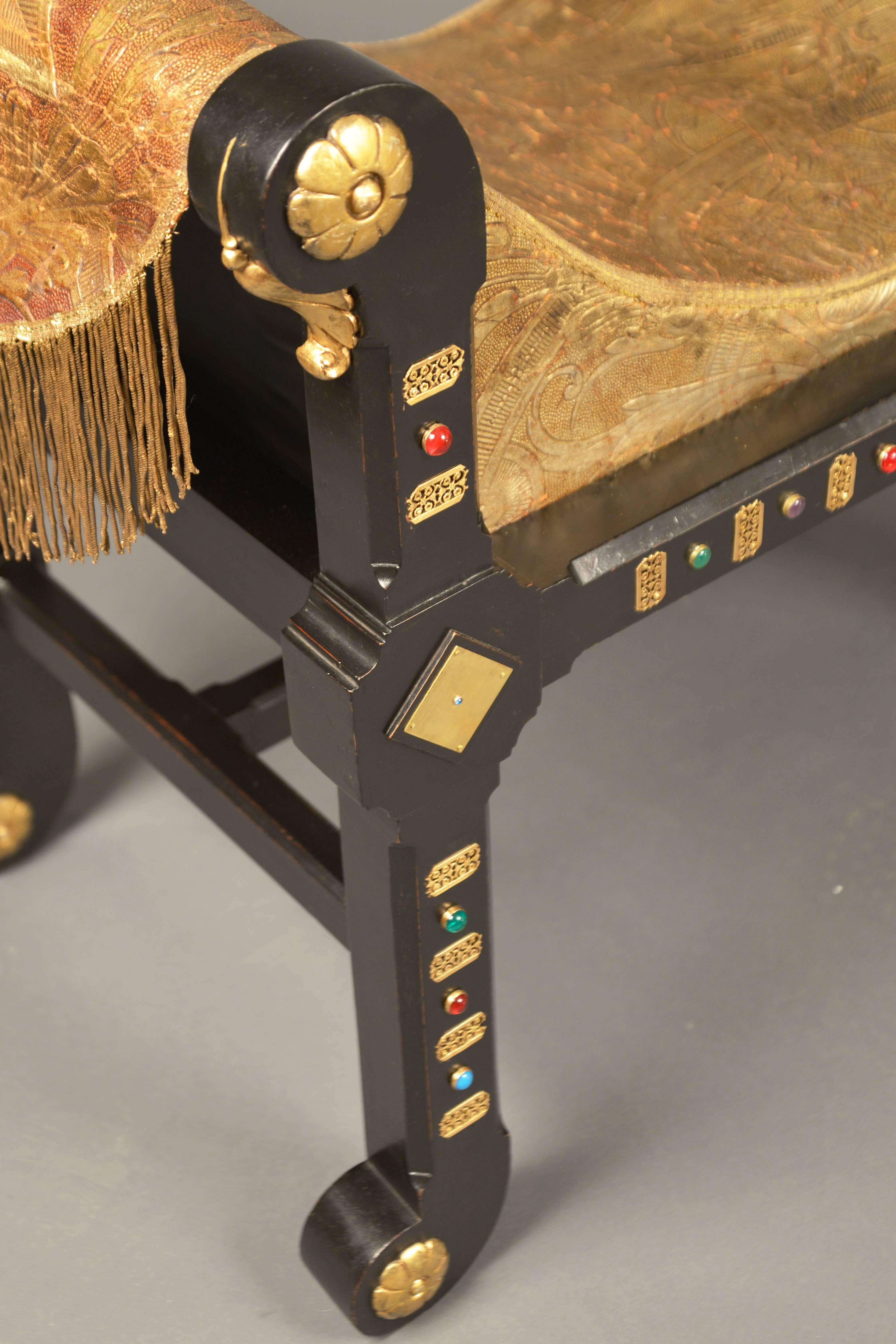 Pair of richly decorated benches in the Egyptian Revival style, made popular after the discovery of King Tut’s tomb in 1922. Ebonized wood with brass decorations and cabuchons throughout, the upholstered seats are covered in painted and embossed