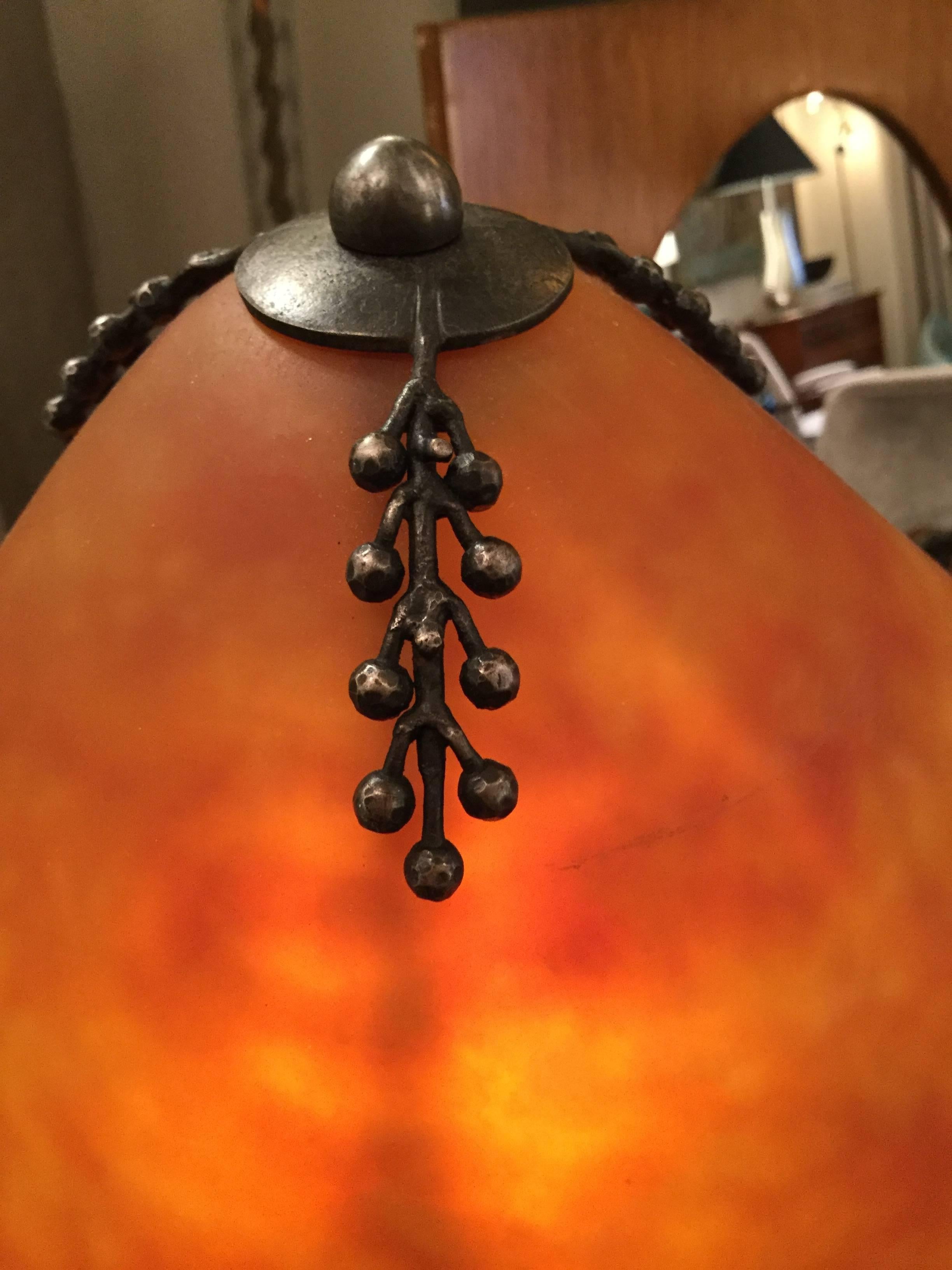 Wrought iron composed of coils and beads on a flattened cone base. Conical lampshade and inner reflector in orange opalescent glass by Daum. Stamped “E Brandt” on foot and etched “Daum Nancy” on the reflector.
Similar model pictured in Clotilde