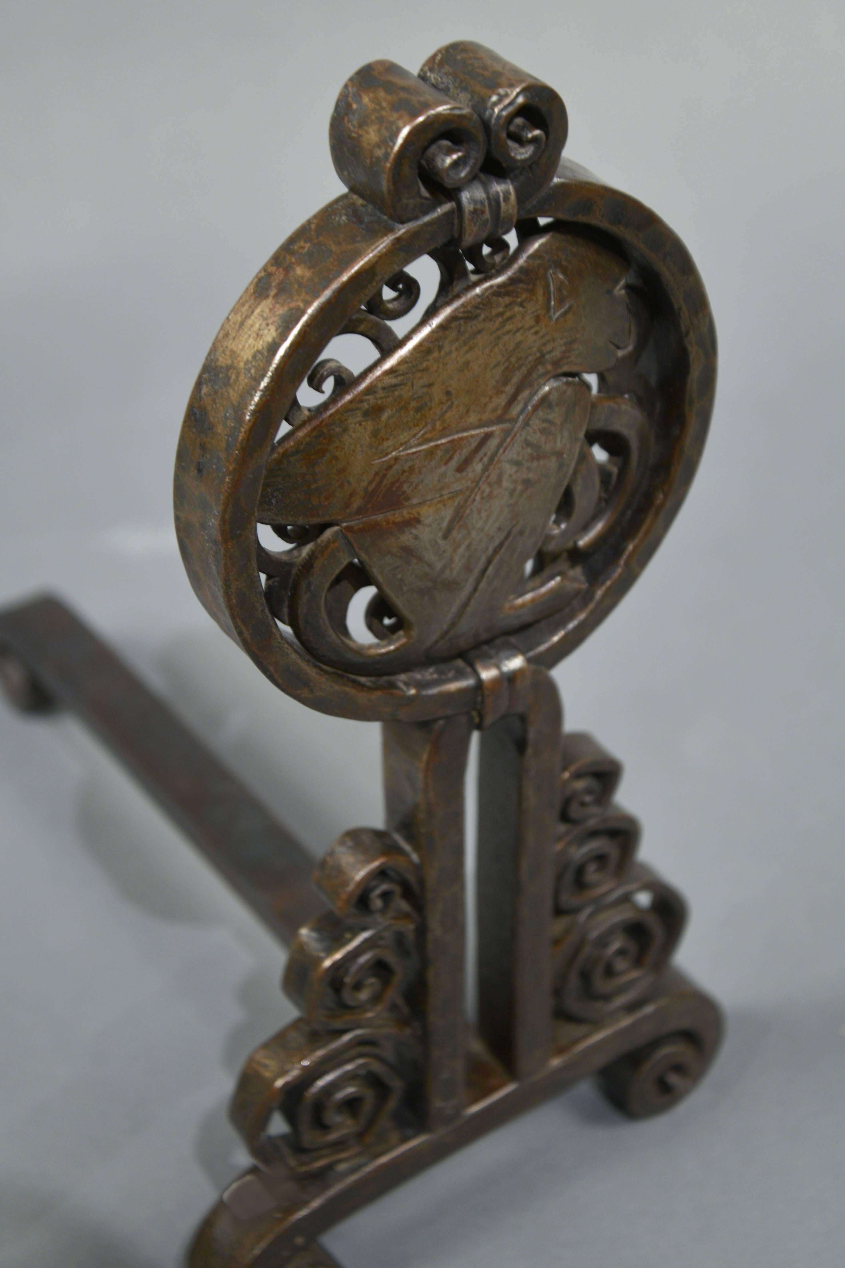 Pair of wrought iron andirons, each featuring a round medallion depicting a crouching monkey, raised on a base with scrolls in varying sizes. One andiron marked “E Brandt”.

  

