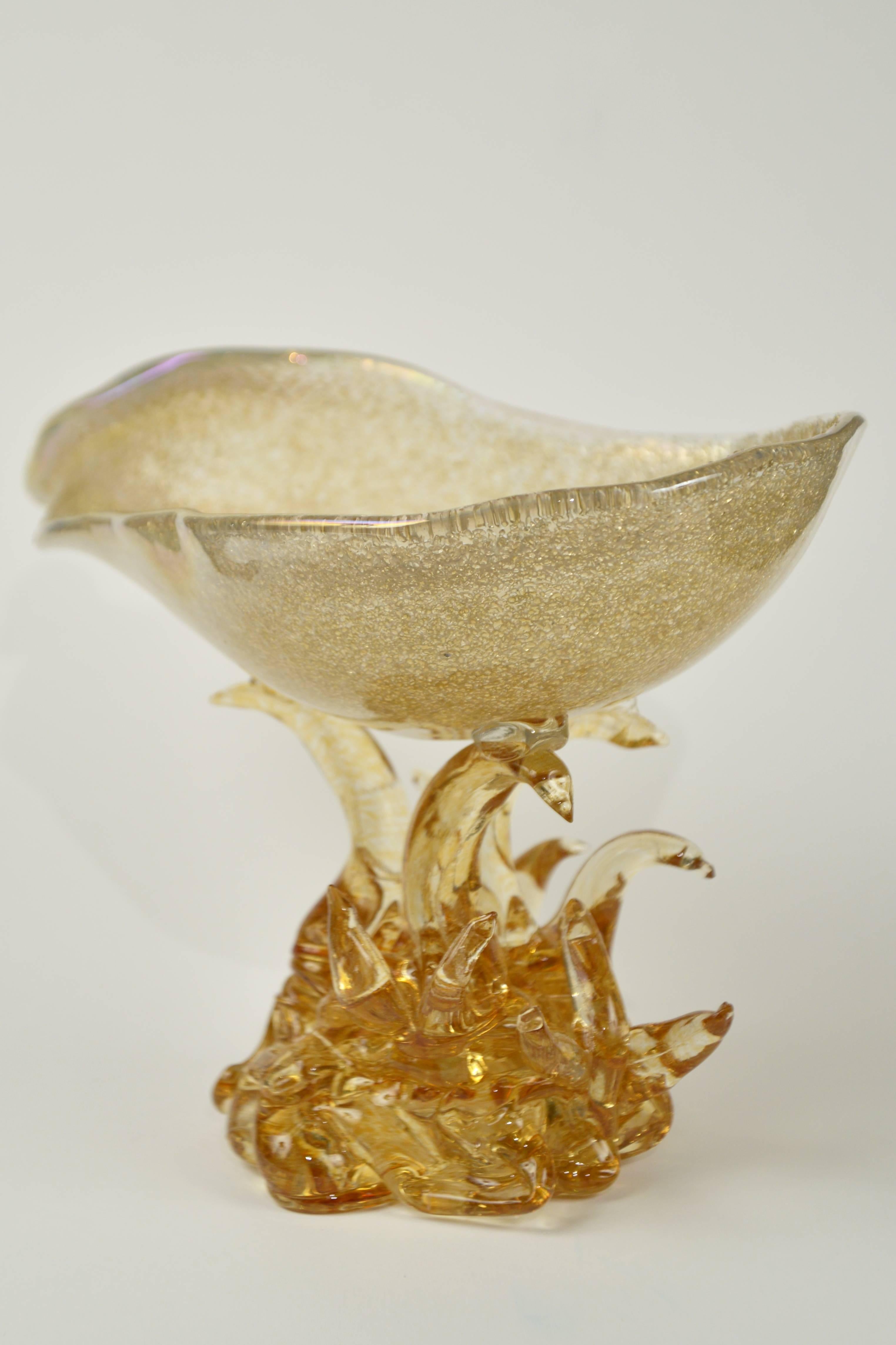 Amber colored “rugiadoso” glass with gold dust inclusions throughout. A seashell-shaped dish held by a stylized algae amber colored glass base. Model “Coppa Rugiada” introduced during the Venetian Biennale in 1940.
Pictured in Leonarde Arte “Il