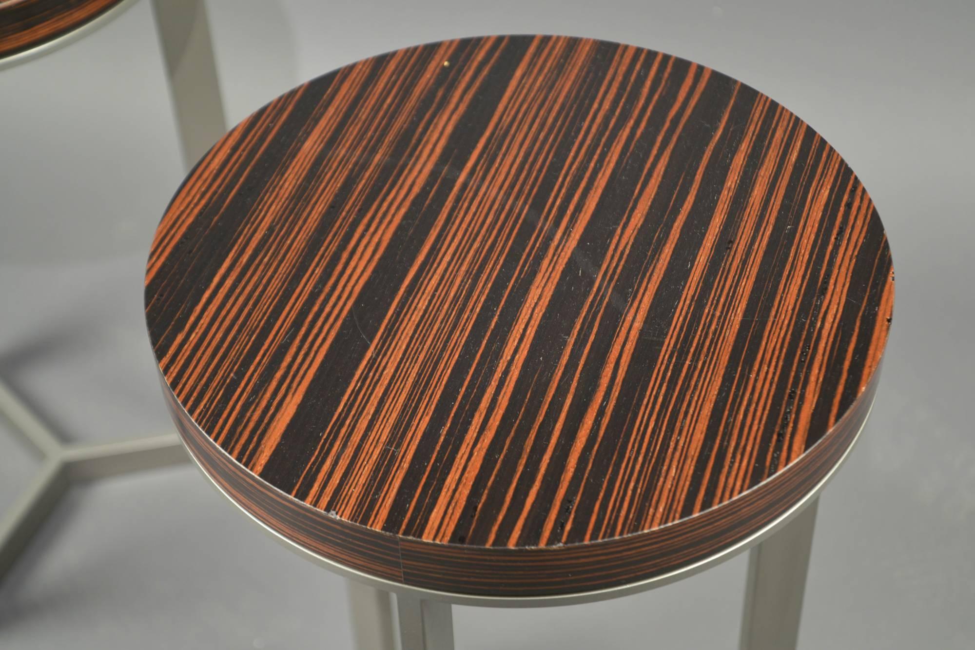 Round steel tables, each composed of three legs, connected by stretchers on the bottom, the top covered with a laminate imitating zebra wood.
   
