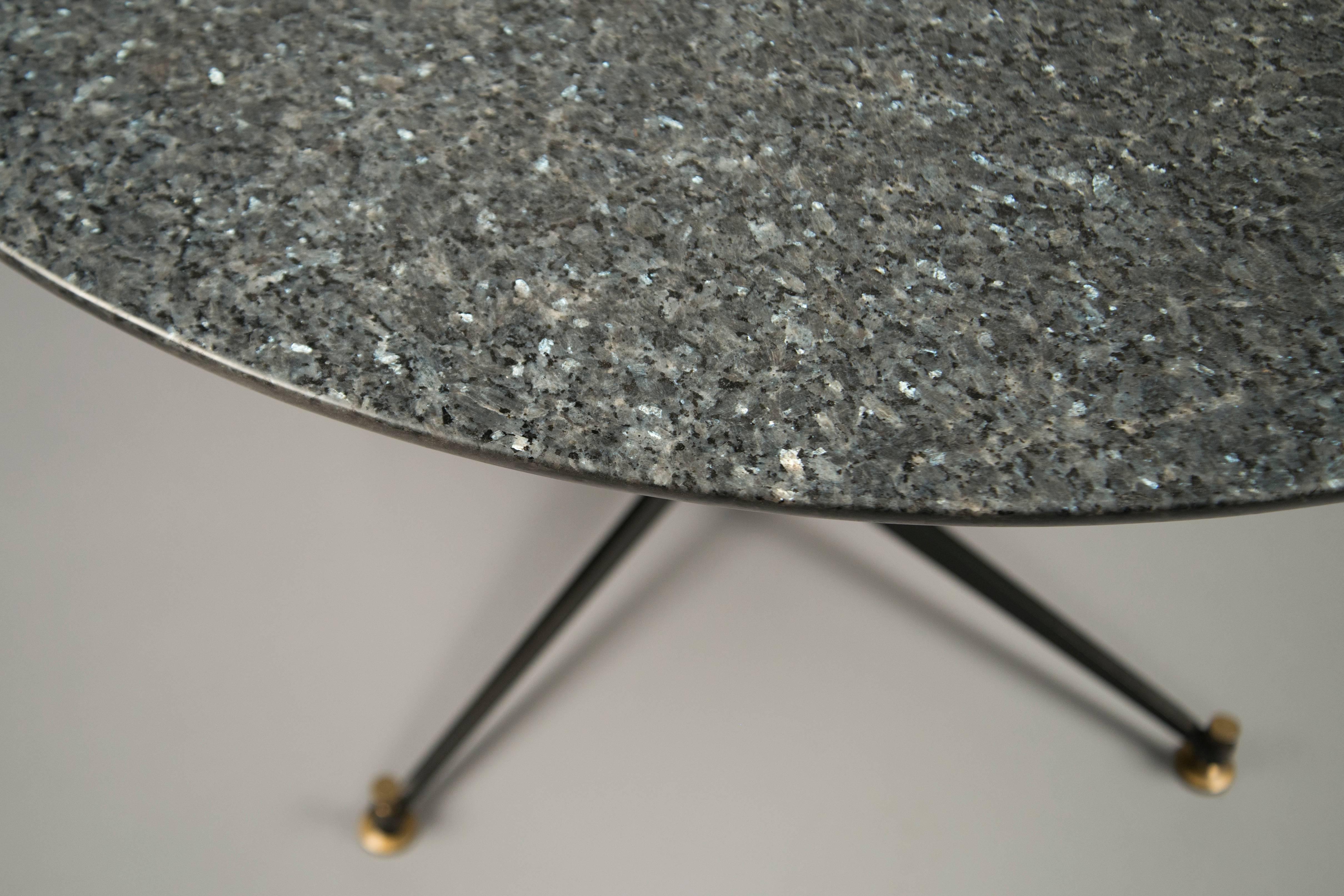 Circular centre table composed of a black metal base with bronze screws and sabots, supporting a gray granite top.
Our number N-10244.