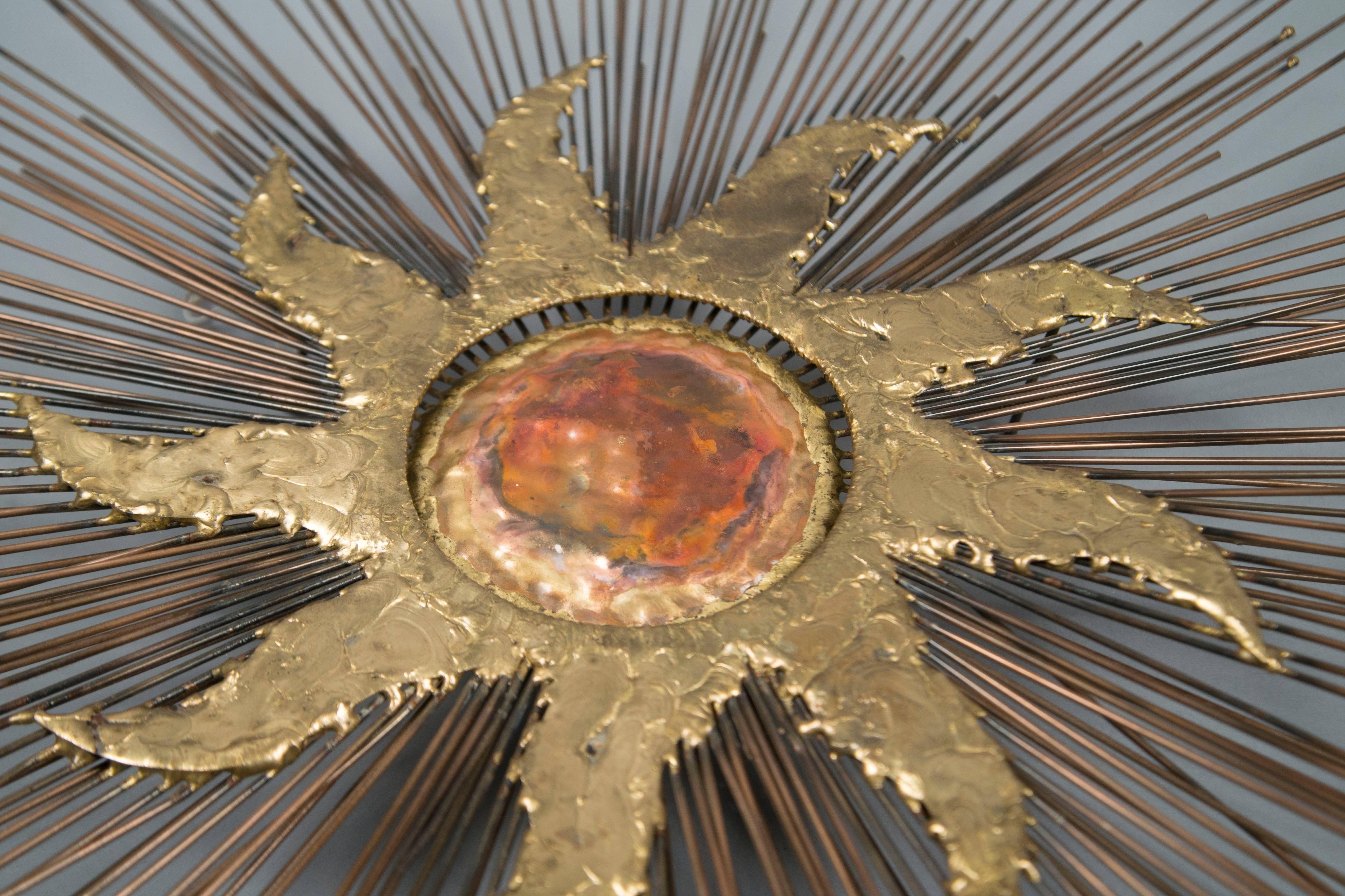 Brass wall sculpture featuring a stylized sun with an oxidized reddish center on top of radiating brass rods of varying lengths.
  
  