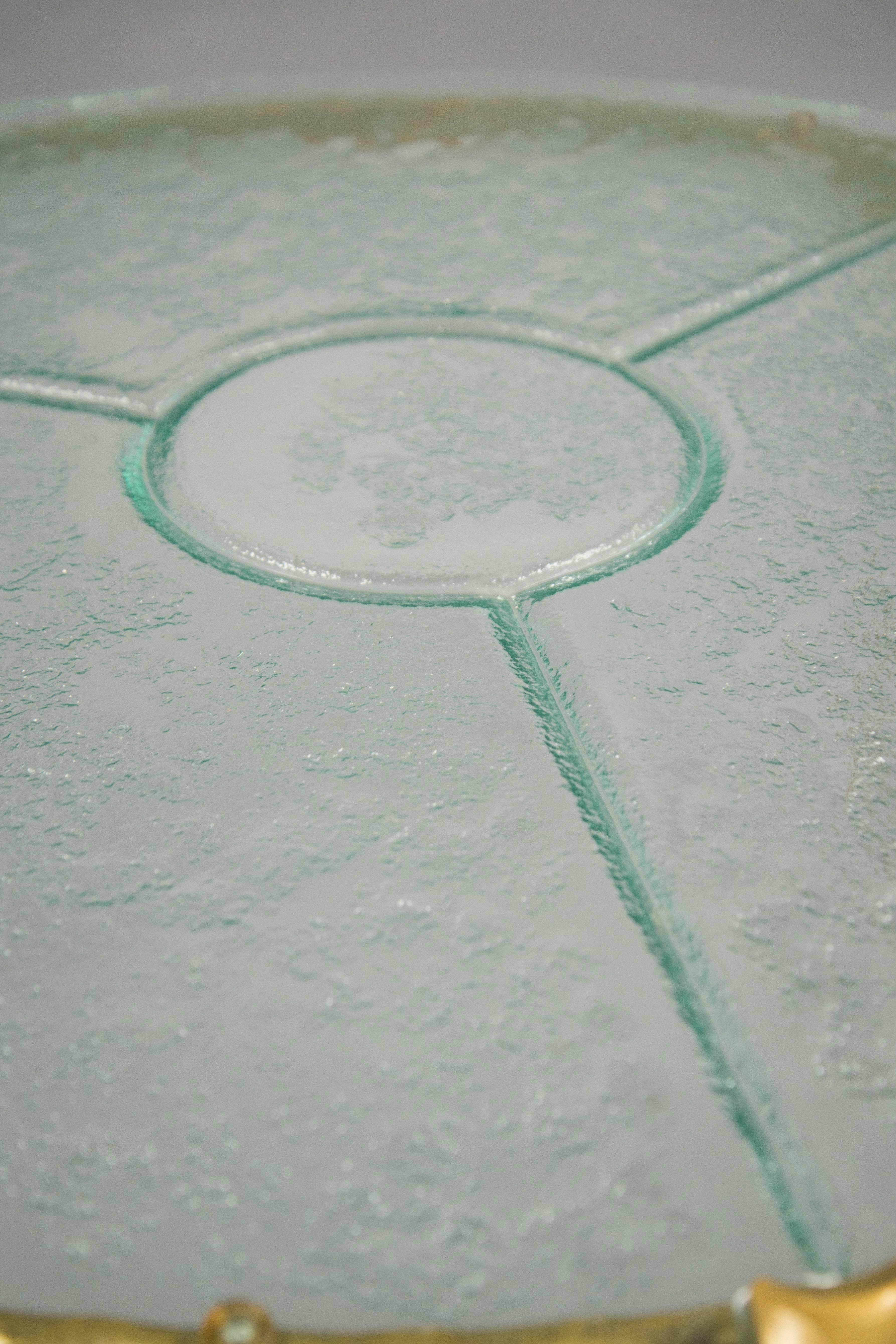 Painted brass and glass coffee table composed of a clear cast glass top, supported by three legs with a hammered structure.

Measures: Height: 21.5” diameter: 42”.