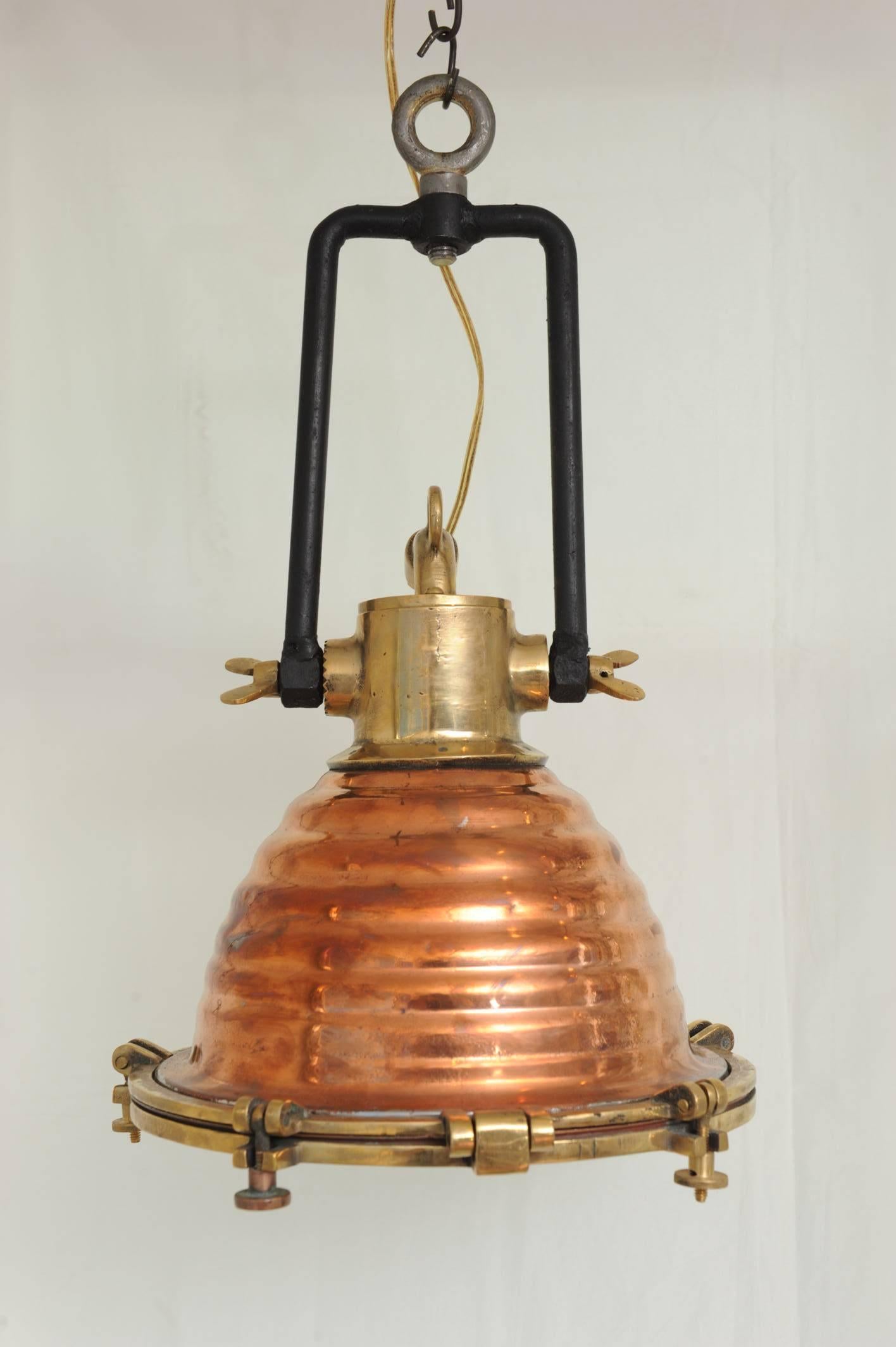 A stunning pair of copper and brass deck lights used on Mid-Century merchant ships to unload cargo at night. The interior is silver-lined to create additional reflective light and they suspended from an adjustable iron bracket. Rewired for American