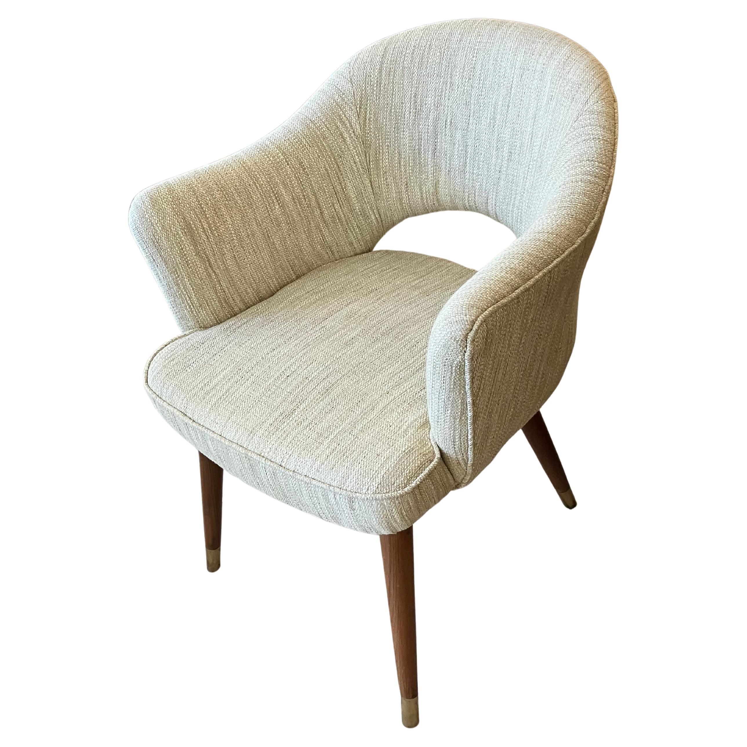 A pair of upholstered Mid-Century Modern tapered-arm barrel chairs.  Teak wood legs with brass feet and a half-moon cut-out back.  Reupholstered in a textured off-white fabric.  Circa 1970's.  Great size and easy to place anywhere.  European.

The