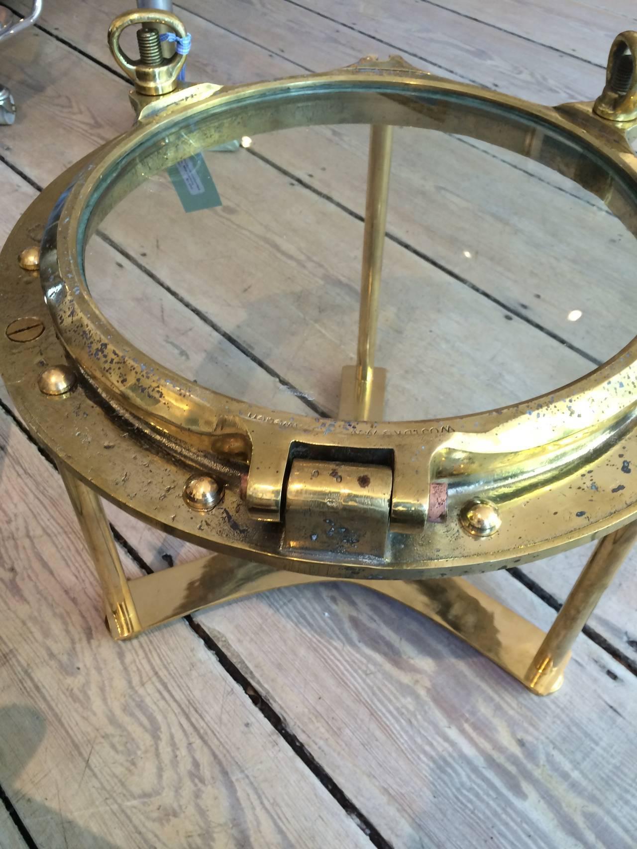 Solid brass working porthole window from a decommissioned ship with great patina. This has been polished, the rivets put back in and a table base designed by us to disassemble if needed. I'll be honest, it's heavy. Use as a side or coffee table,