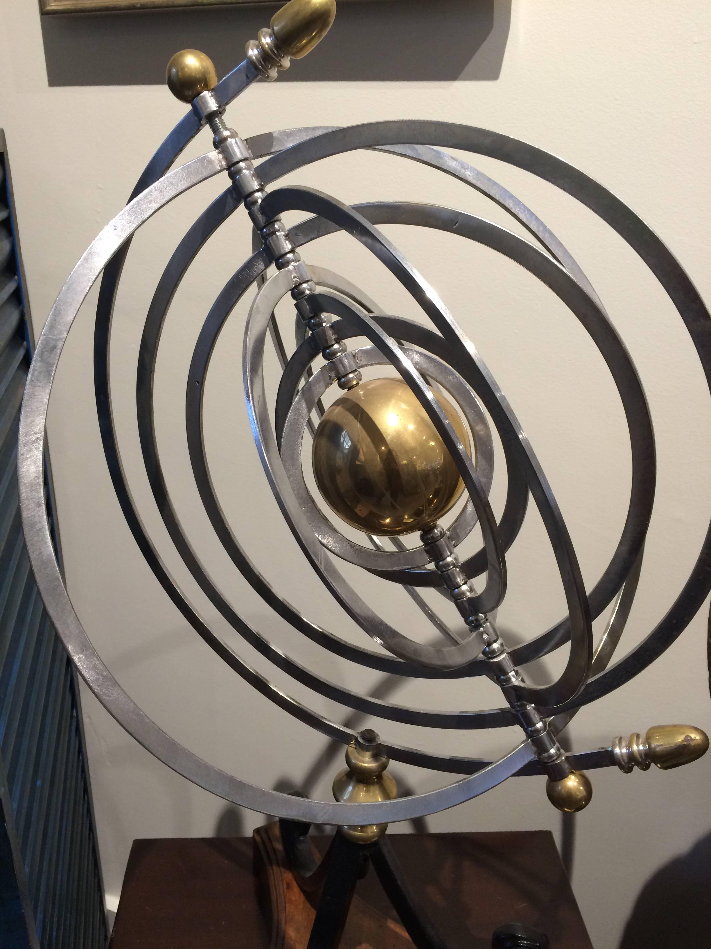 Celestial chrome armillary with a brass centre representing the sun and chrome orbital rings of the nine planets that move creating a dimensional affect or lay flat. Mounted on a black iron stand and teak wood base, circa 1970s-1980s.