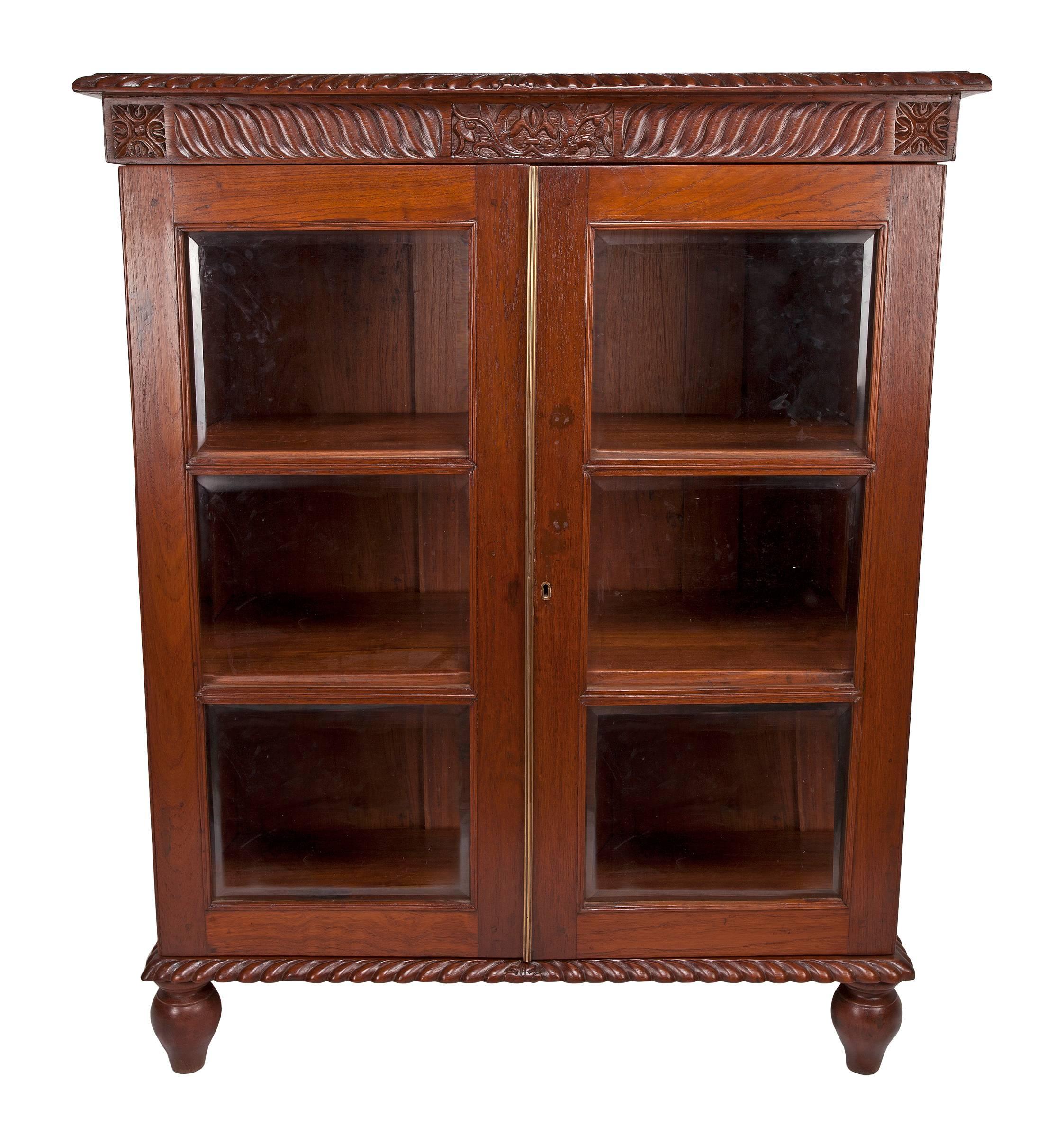 Lovely British Colonial mahogany petite size bookcase with glass door panels and interior shelving. Lovely gadrooned-carved edging along the cornice and the apron. Working lock and key. Great size and elegance for easy placement in a room. The width