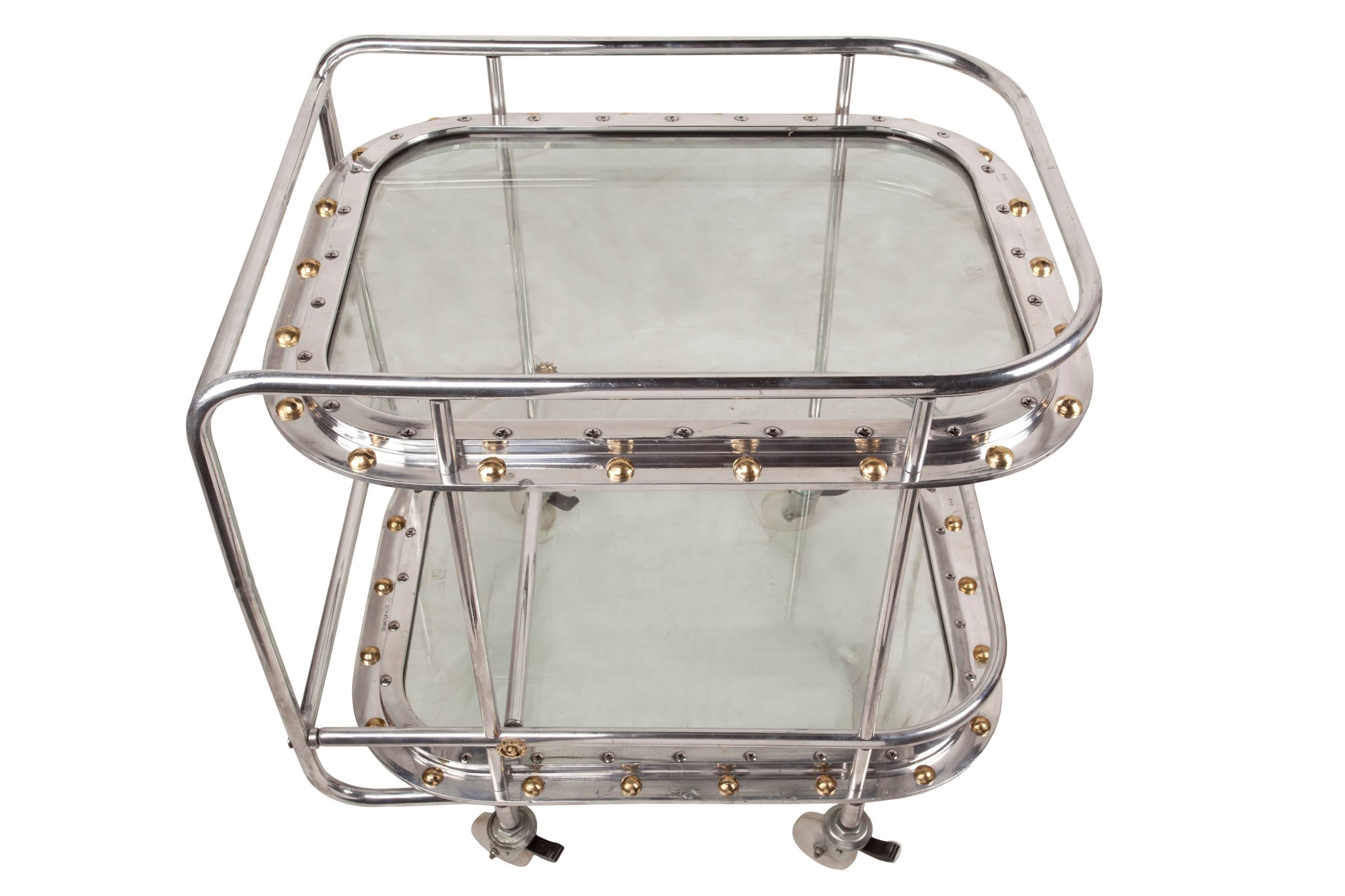 A bespoke piece, using two original 1970s chrome porthole windows with brass rivets returned instead of the normal chrome ones (the original rivets pop out when ship's are dismantled), and then fashioned into a bar cart. Full round wheels replace