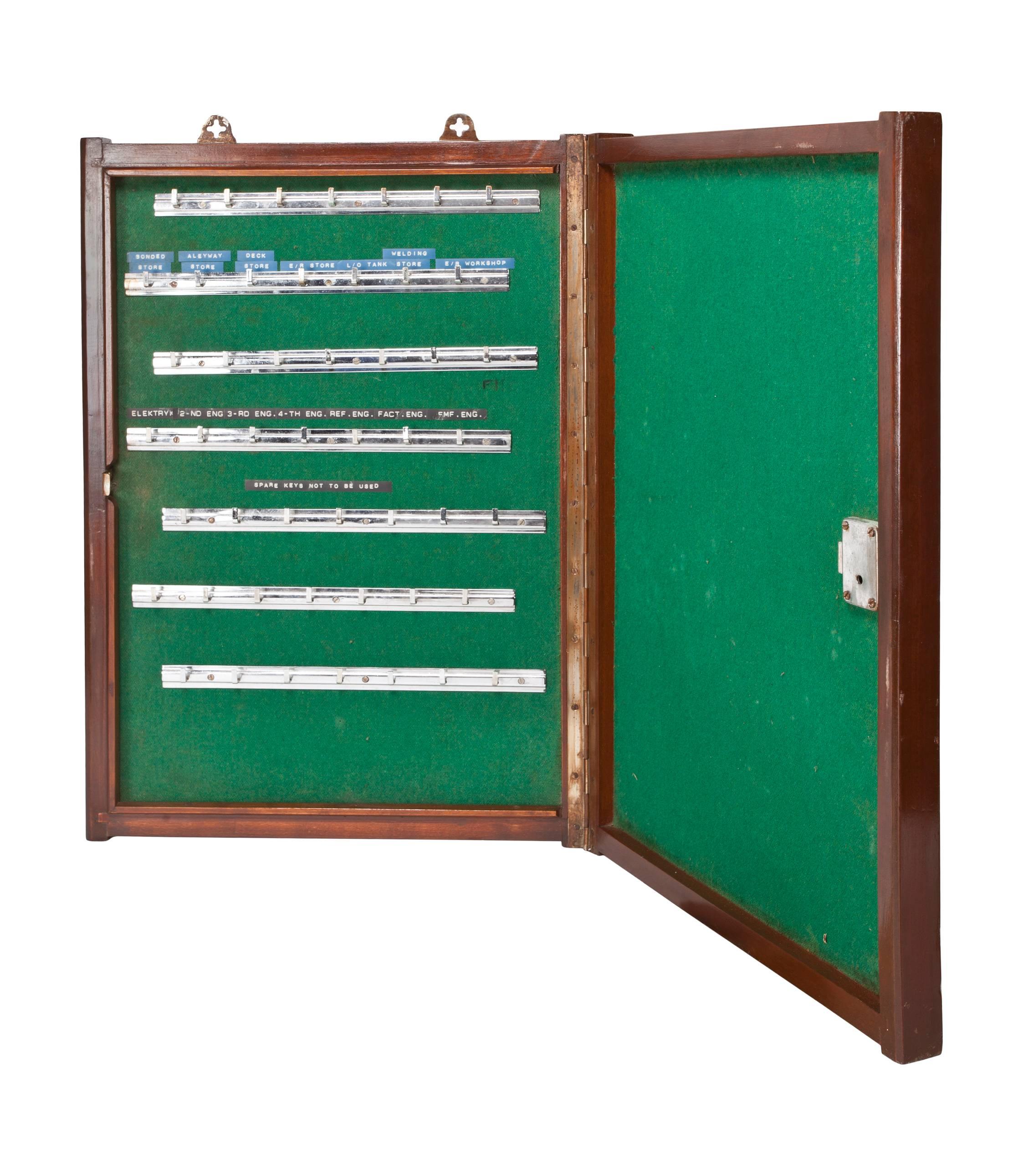 A teak key storage cabinet lined with green felt and chrome hooks. The front door closes and locks. From a decommissioned ship, circa 1970s. A rare find. Complete with lock and key and mounting brackets and the original embossed key labels.