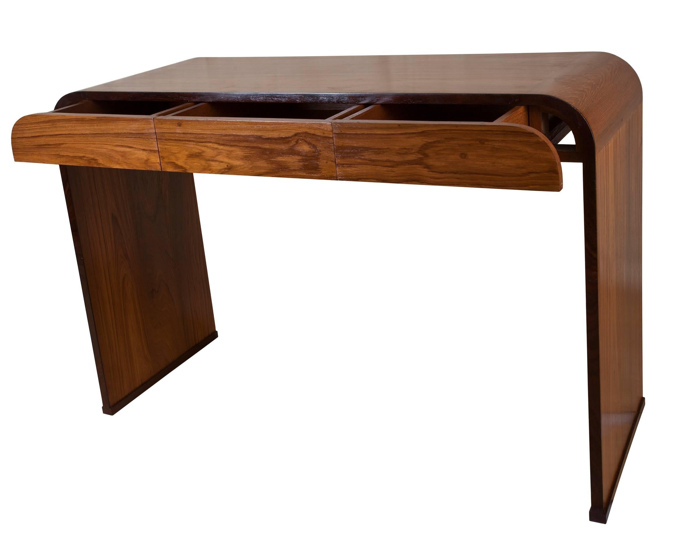 Mid-Century Modern 'waterfall' desk made of teak with rosewood borders. Three front drawers, the two on the sides have rounded corners. Refinished. Great to use as a desk, console or sofa table. Elegant lines and lovely wood grain. Height from the