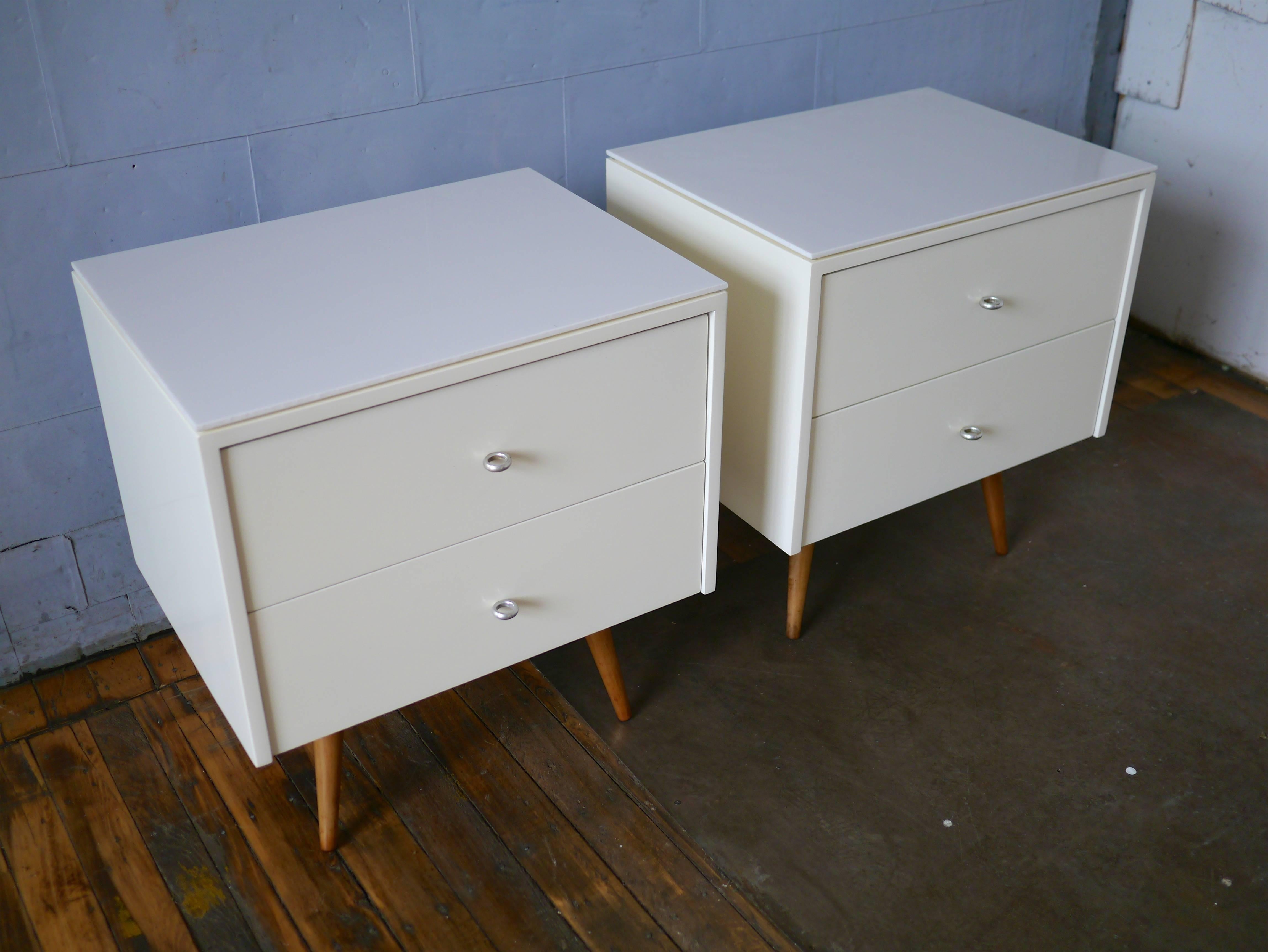 Nightstands designed by Paul McCobb for his planner group line. These examples have two drawers, ring pulls and have been redone in white lacquer. The vitrolite glass tops were an option for earlier Planner Group pieces. Also known as Carrera glass,