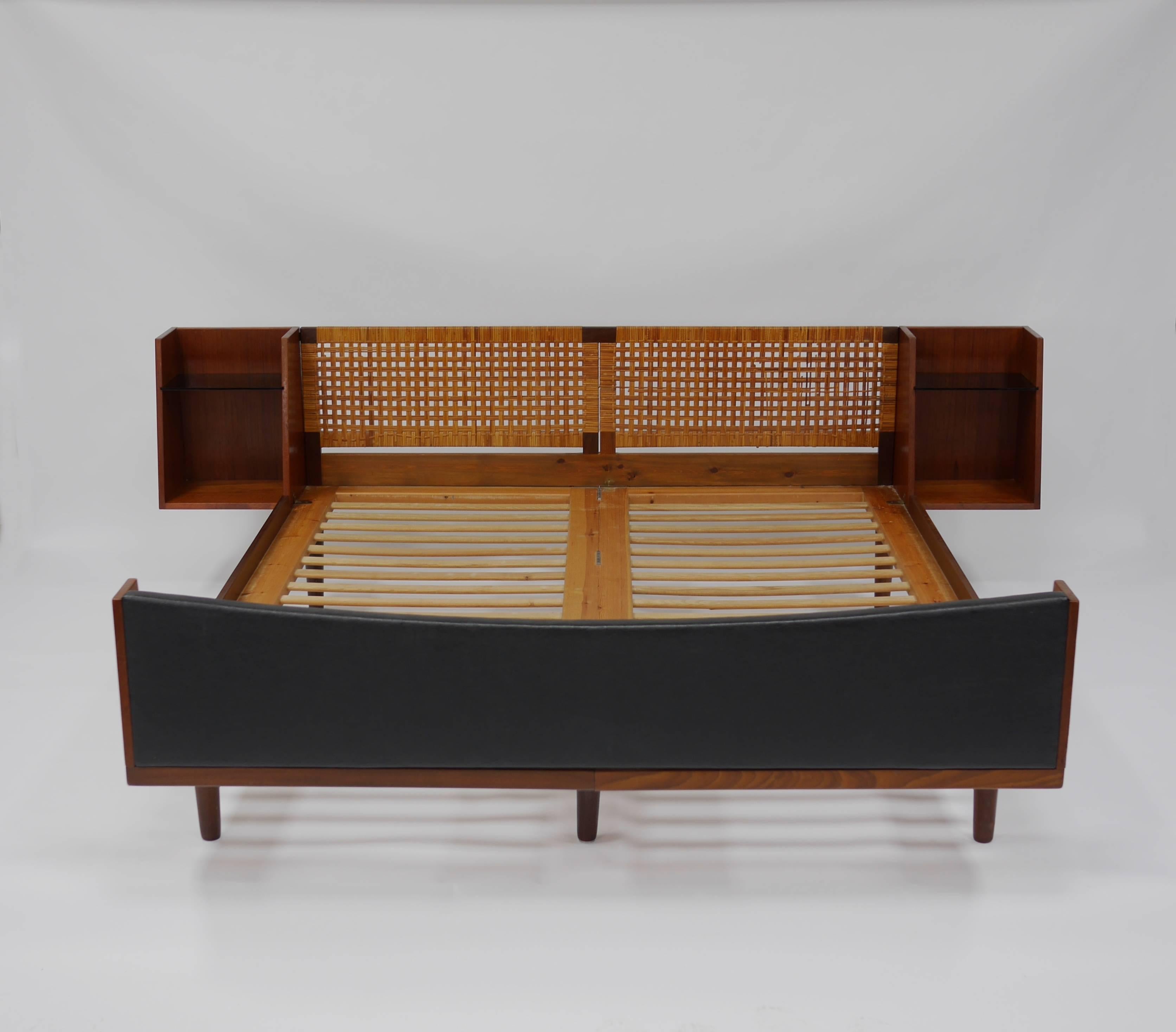 Queen-size bed model 701 by Hans J. Wegner for GETAMA. Having a teak timber frame, pine slates, attached nightstands with Vitrolite shelves, caned headboard and a vinyl footboard. Branded mark, Hans Wegner, GETAMA.

Measures: 95