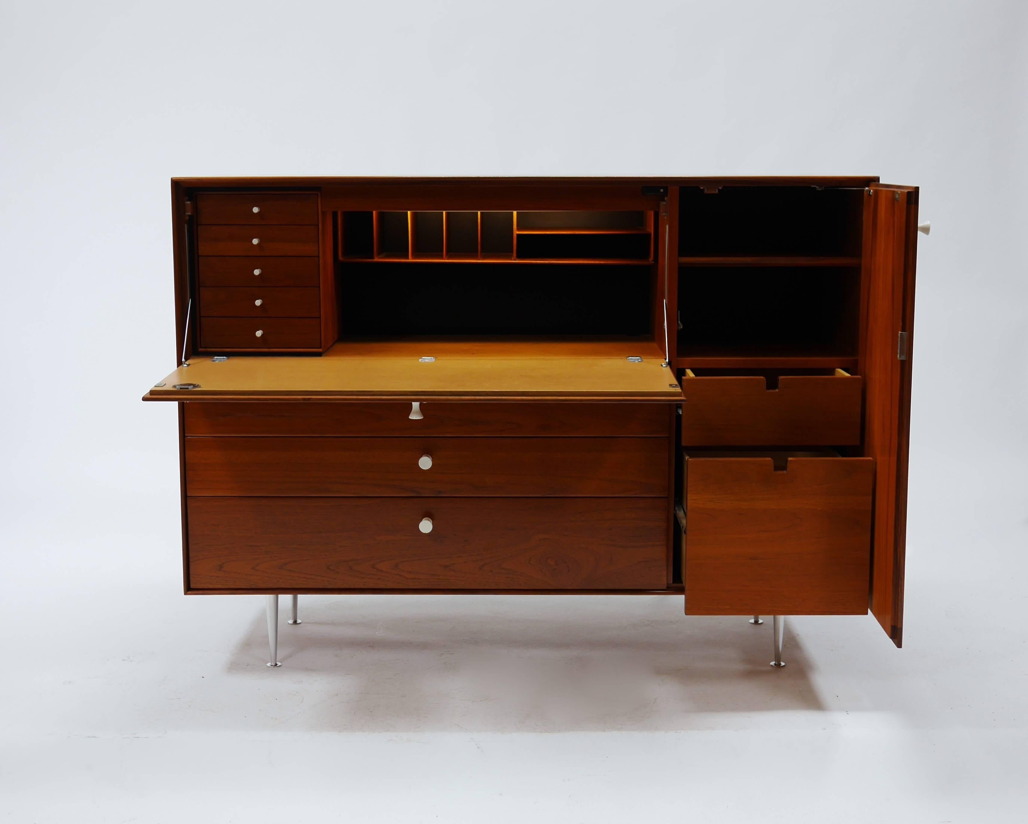 Beautiful secretary or storage cabinet/ desk by George Nelson for Herman Miller. Large-scale cabinet in walnut veneer, raised on turned aluminum legs. Three deep drawers, and a hinged door concealing open shelves and a single drawer. The drop front