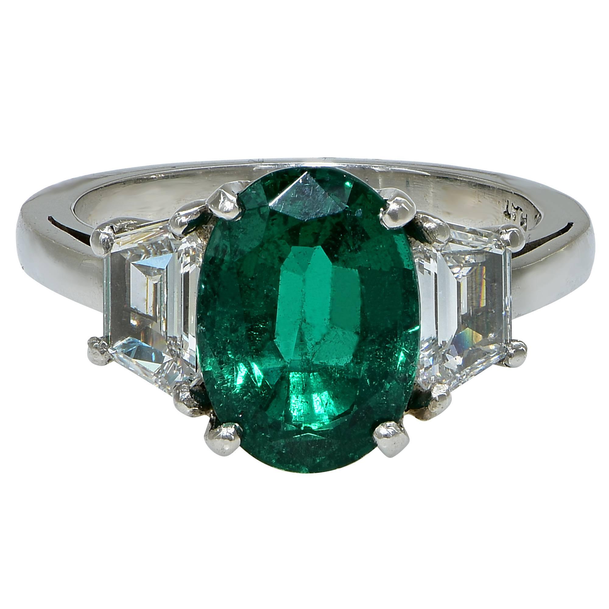 Beautiful rich green AGL graded 2.75ct oval cut emerald flanked by two trapezoid cut diamonds set in a modern platinum engagement ring.

The ring is a size 6.5 and can be sized up or down.
Measurements are available upon request.
It is stamped