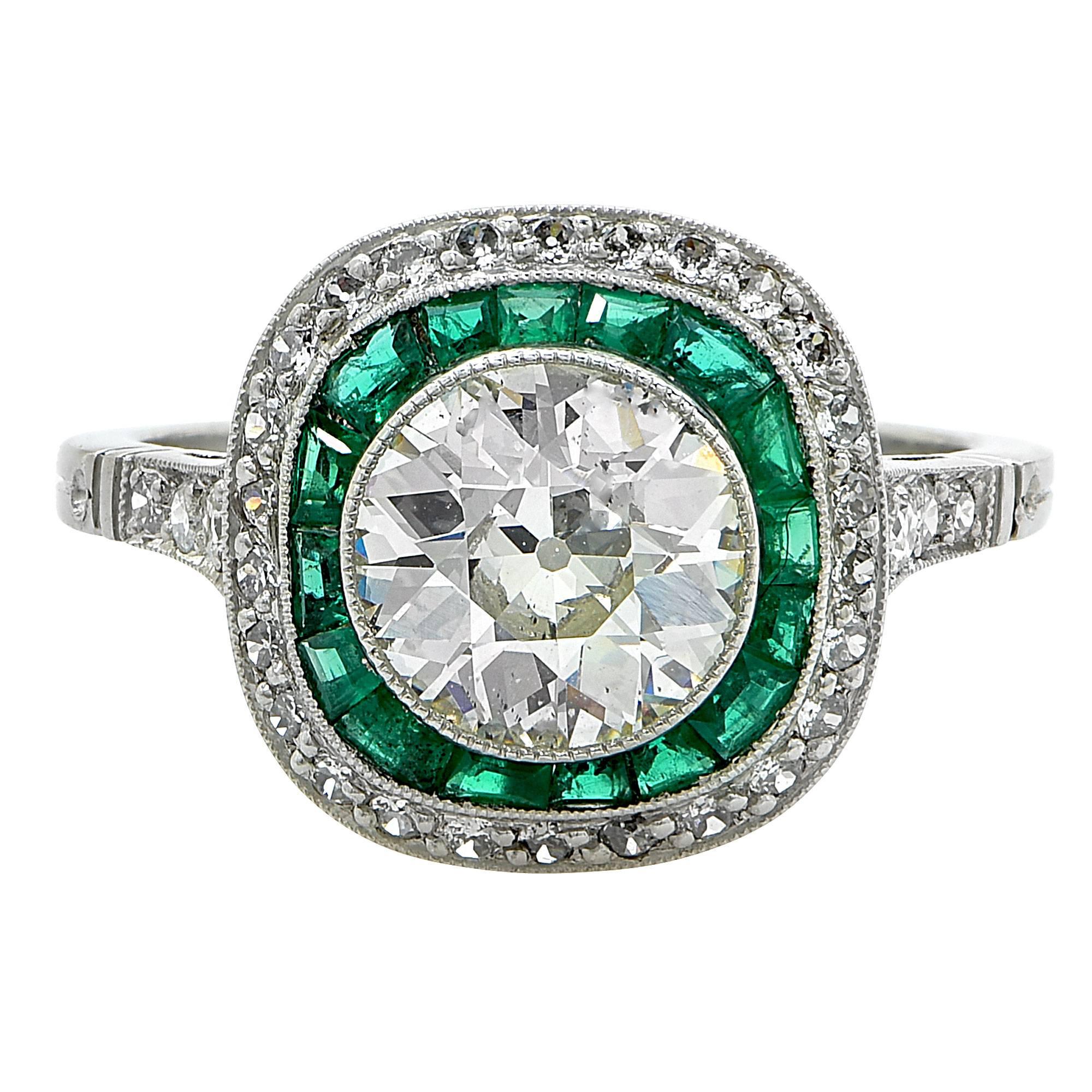 Platinum Art Deco Ring containing a 1.80ct European cut diamond, H color, SI2 clarity, surrounded by 16 vibrant green emeralds custom cut to accent the center diamond. The ring is further accented by the hand cut filigree on the gallery.

Ring