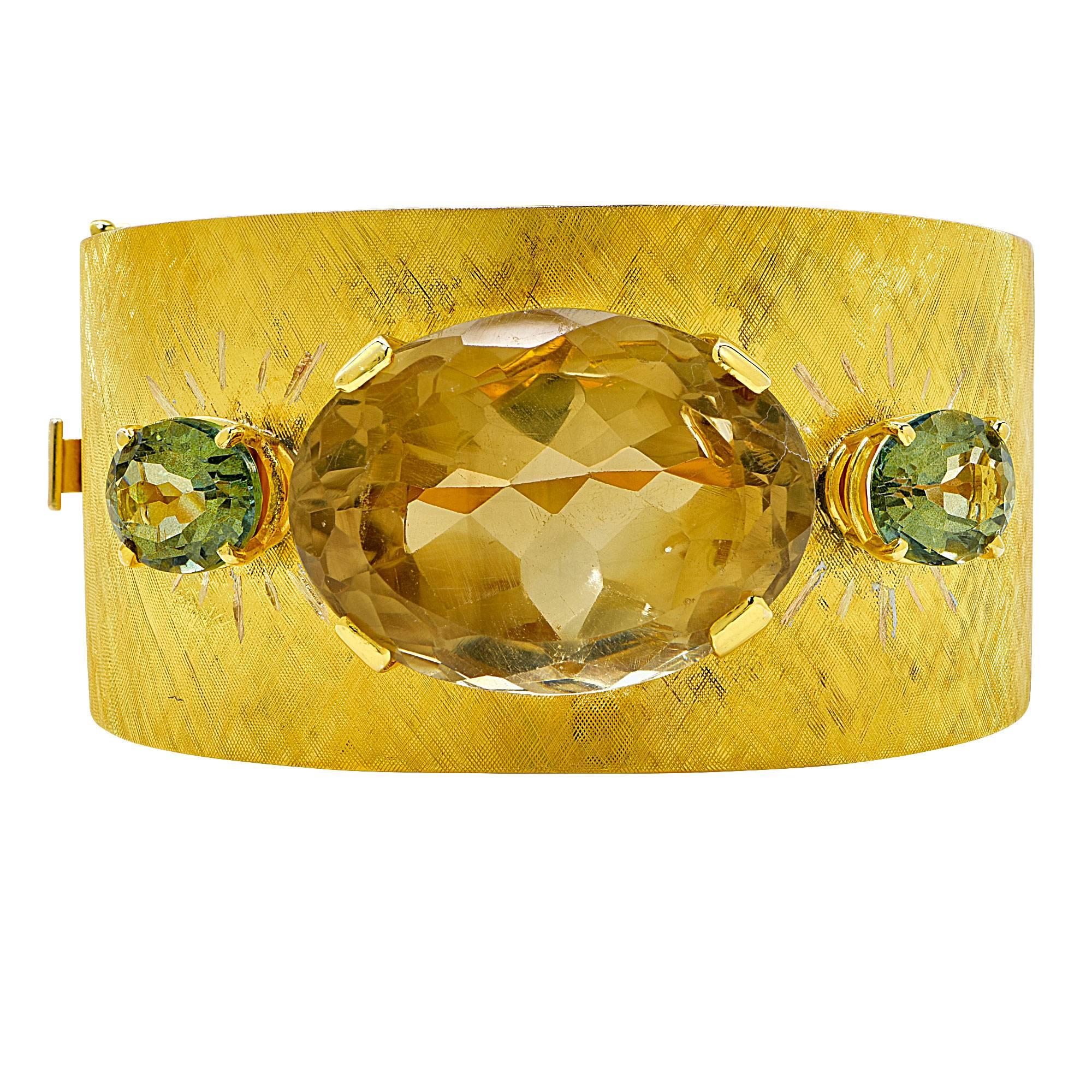 14k yellow gold bangle featuring an oval cut Smokey Quartz weighing approximately 80cts total accented by 2 oval cut green tourmaline weighing approximately 8cts total.

The bracelet measures 36.5mm wide
It is stamped and tested as 14k gold.
The