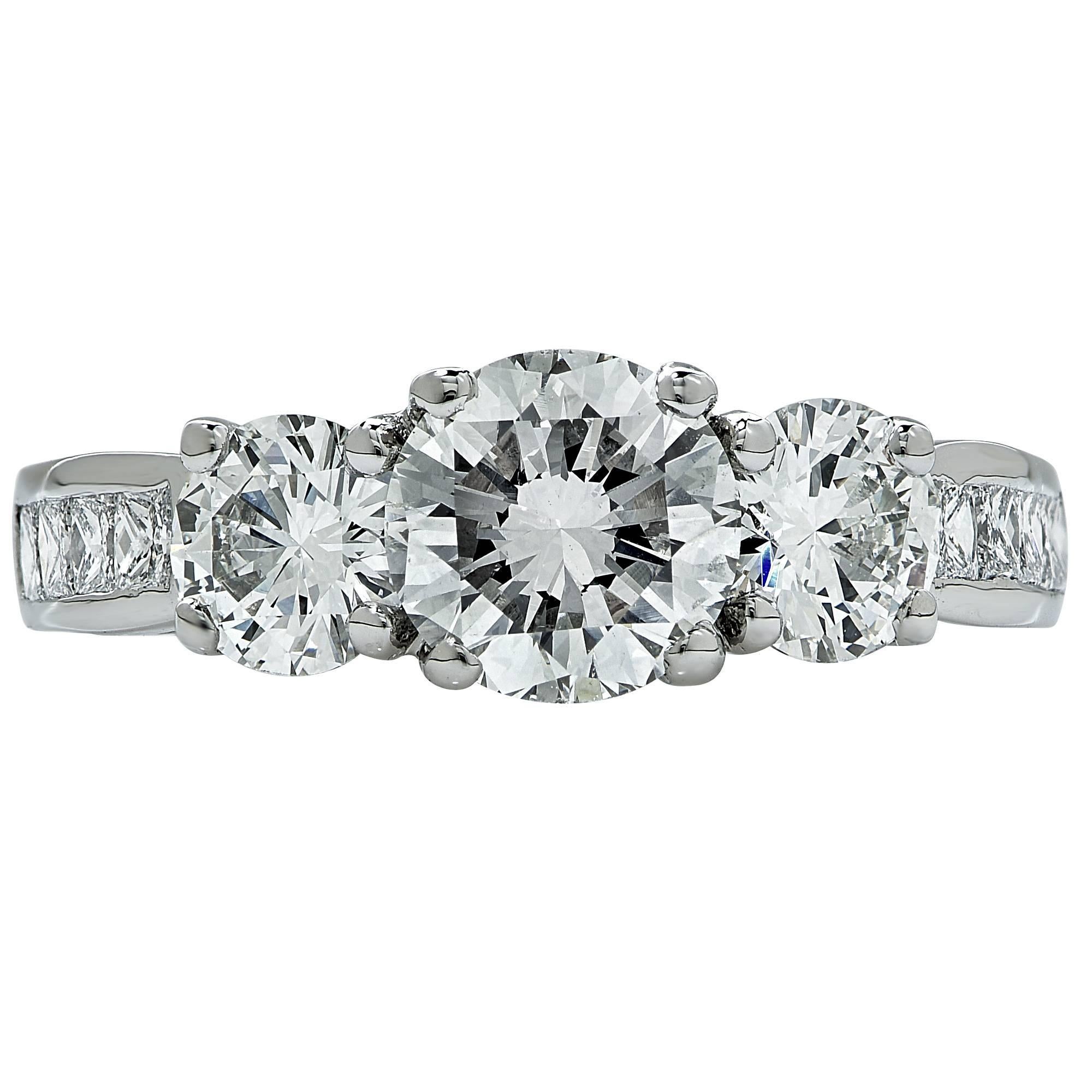 Platinum engagement ring features a 1.06ct H SI1 round brilliant cut diamond flanked by 2 round brilliant cut diamonds weighing .80cts H color and VS clarity. The ring also is accented by 8 princess cut diamonds weighing .32cts H color VS
