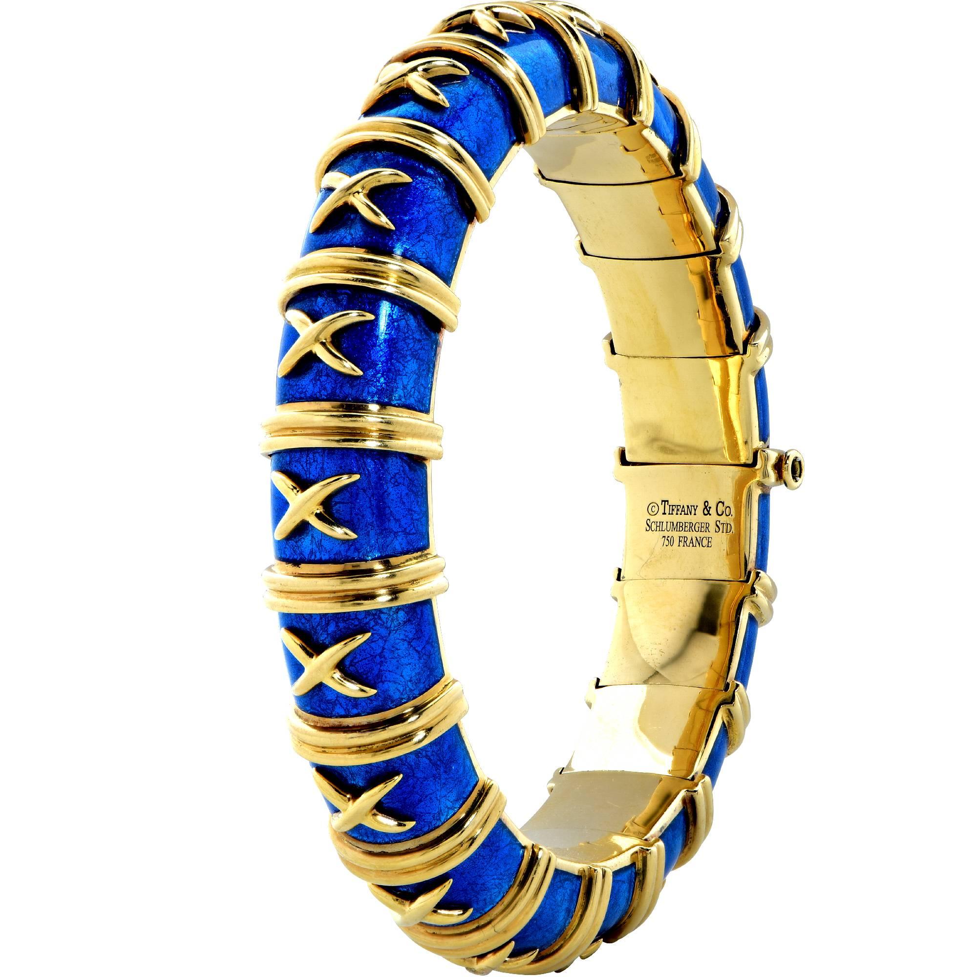 Stunning Tiffany & Co. Schlumburger bangle, crafted in 18k yellow gold and enrich with electric blue enamel, accented with gold X’s and double piped borders surrounding the entire bracelet. The bracelet measures one half inch in width and four
