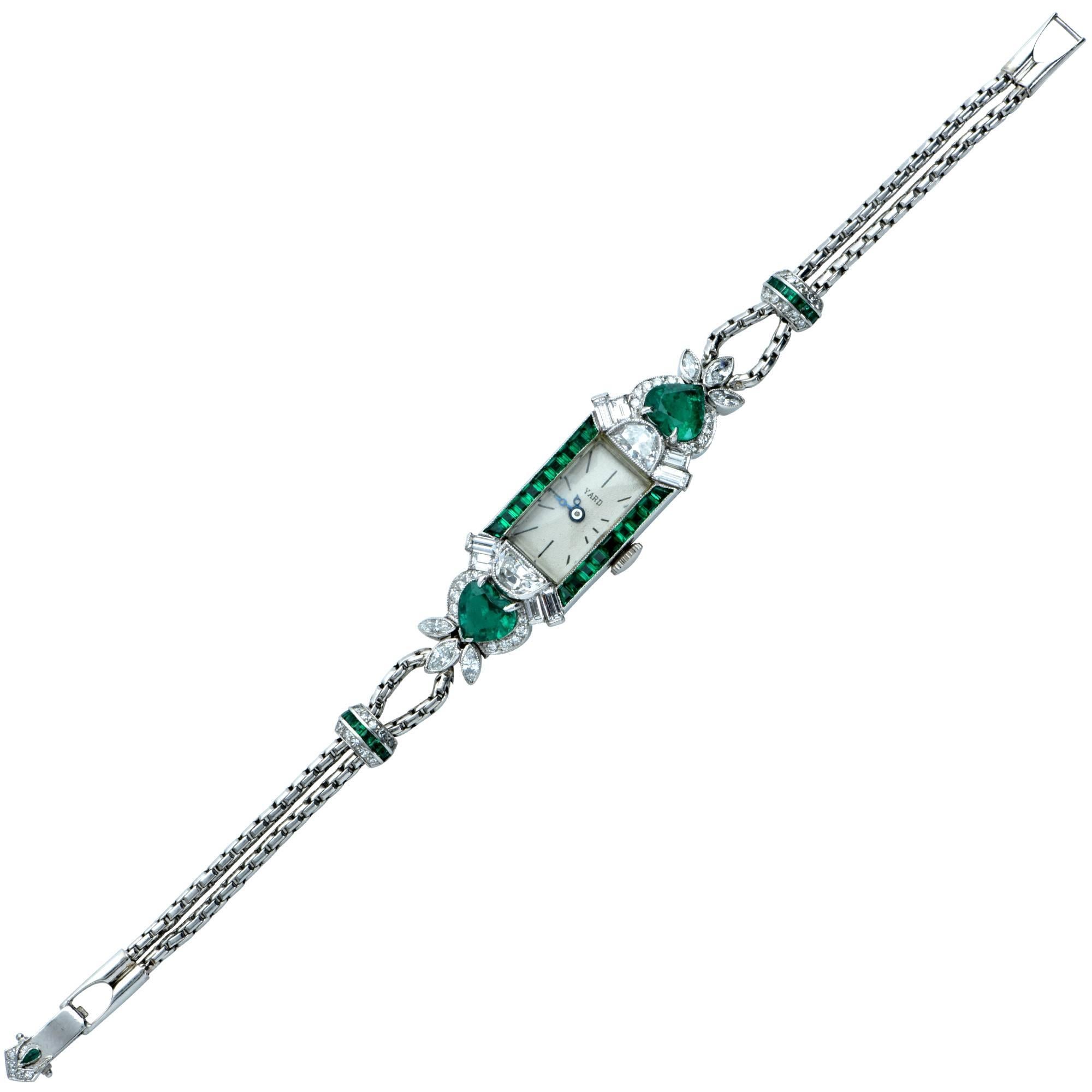 Raymond Yard platinum and diamond watch showcases two beautiful natural heart shape emeralds weighing approximately 2.50cts total and 30 emeralds weighing approximately 1.70cts total. Further accenting the emeralds are 64 mixed cut diamonds weighing