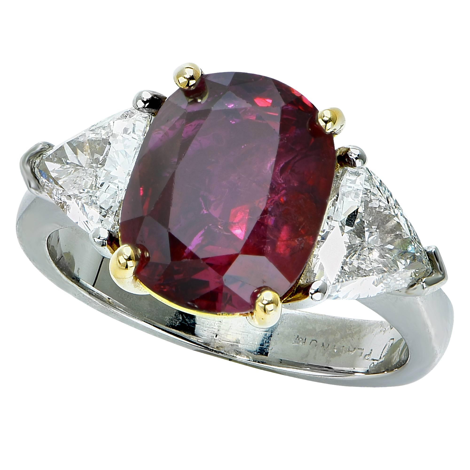 Spectacular engagement ring crafted in platinum and 18 karat yellow gold, showcasing a sensational GIA Certified unheated cushion cut ruby weighing 5 carats, accompanied by two trilliant cut diamonds weighing approximately 1.40 carats total. This