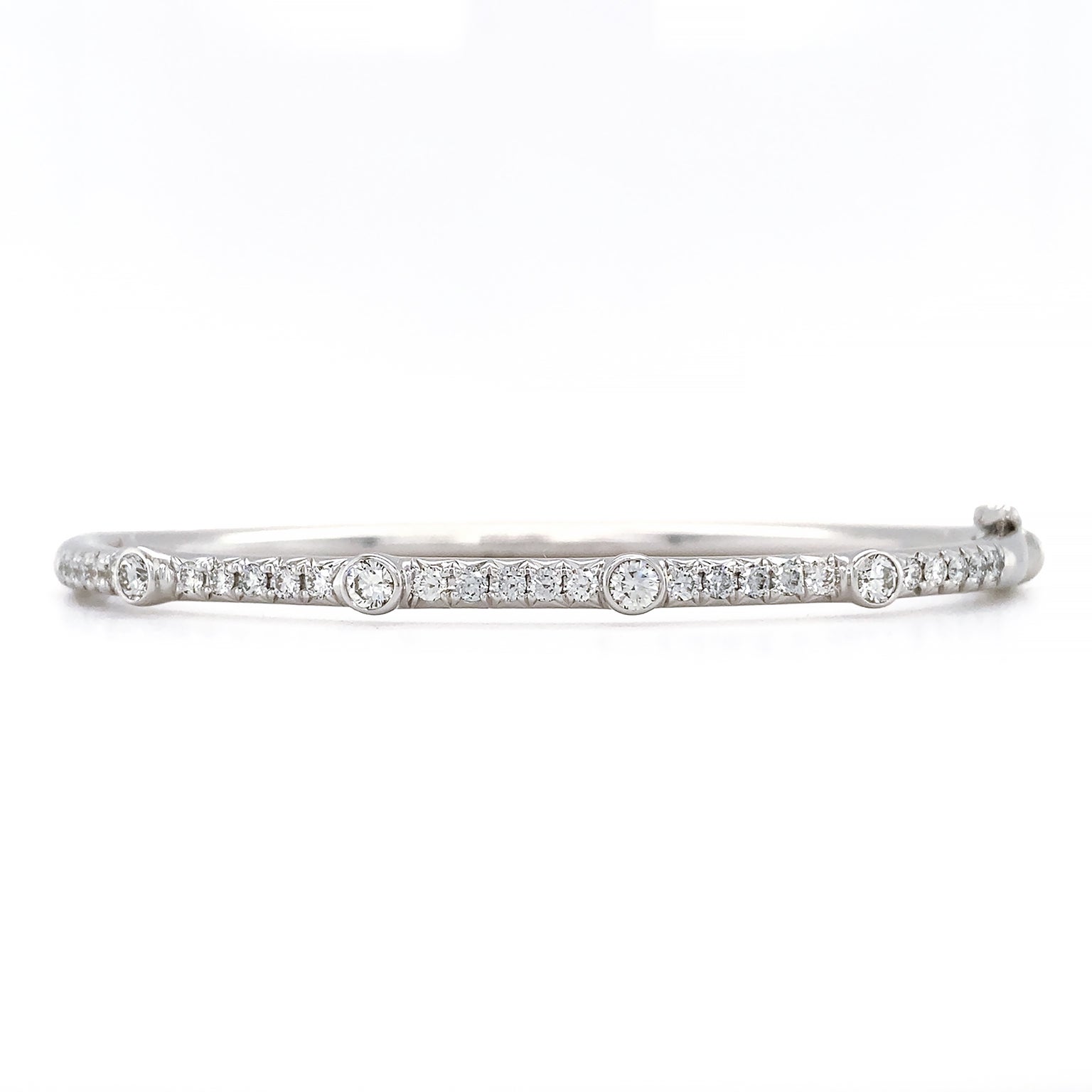 Radiance encompasses this bracelet. A slender 18k white gold bangle is elevated by a row of paved brilliant cut diamonds on the upper part. Four larger bezel set diamonds are dispersed throughout the line. This totals to .99 carats of the gem. A