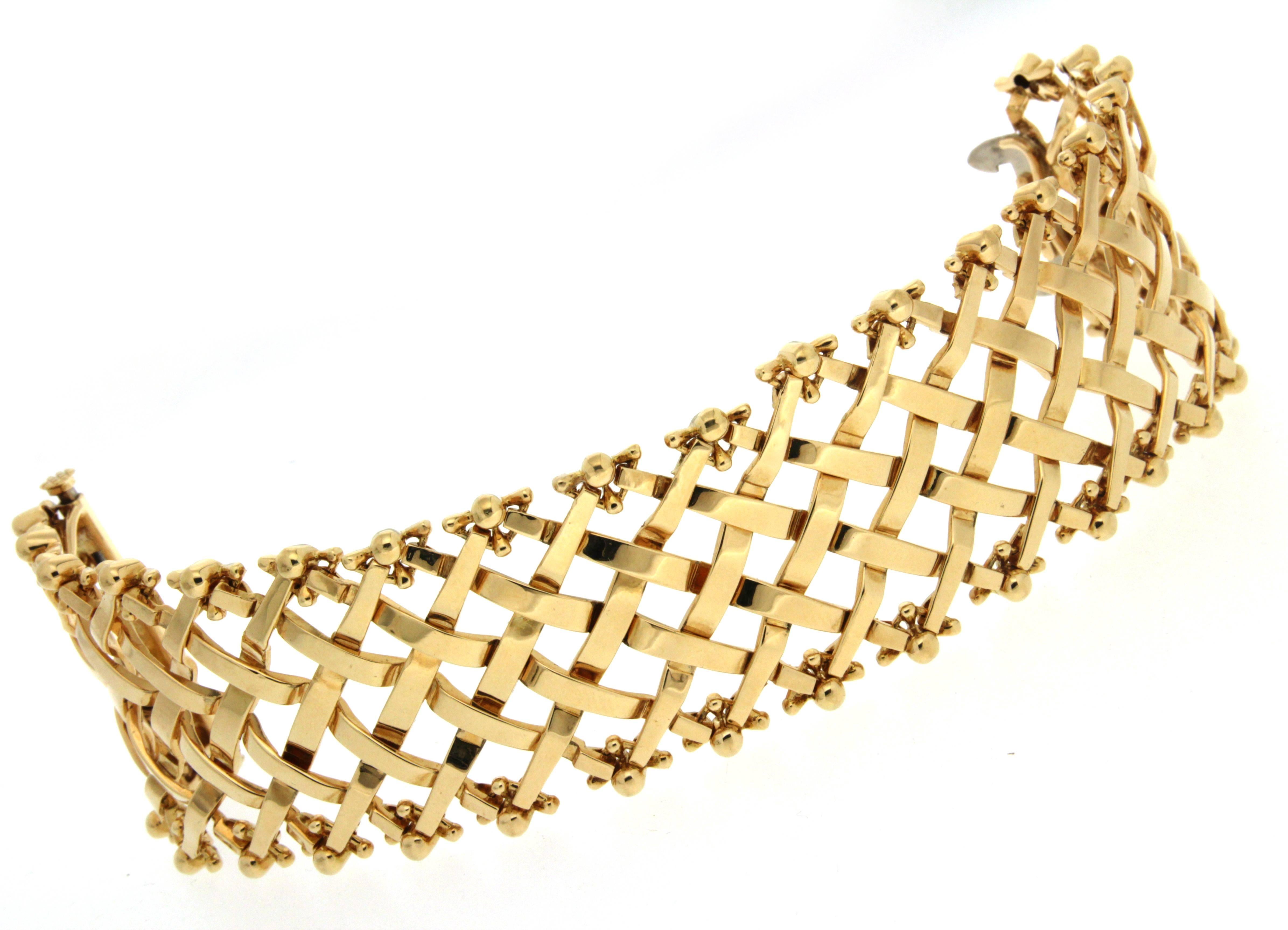 This strap bracelet created by Valentin Magro, boasts a lattice motif. The angled 18k yellow gold strips weave in and out of one another. Tips at the edges of the design boast ball designs of still more gold. A concealed sliding double clasp