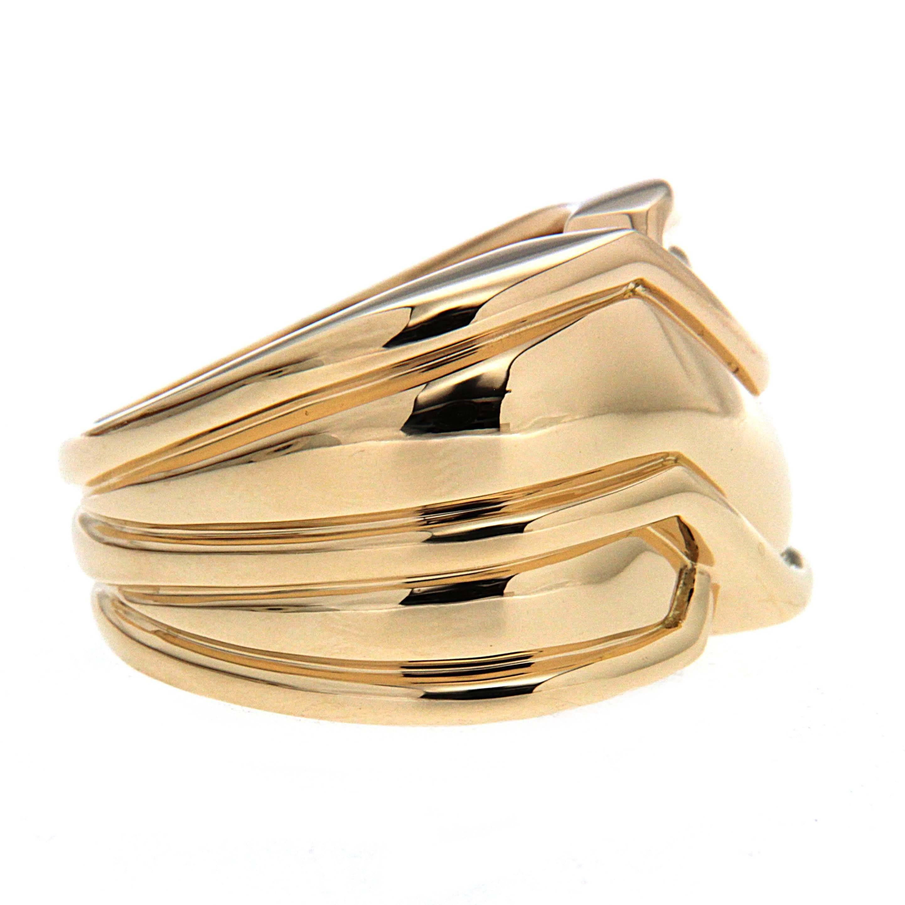 This 18k yellow gold ring concentrates on sleek lines and high polish. The design resembles two side by side bands, each with a groove along their edges. On the knuckle side of the hand, one shank crosses over the other, forming an X. The ring is
