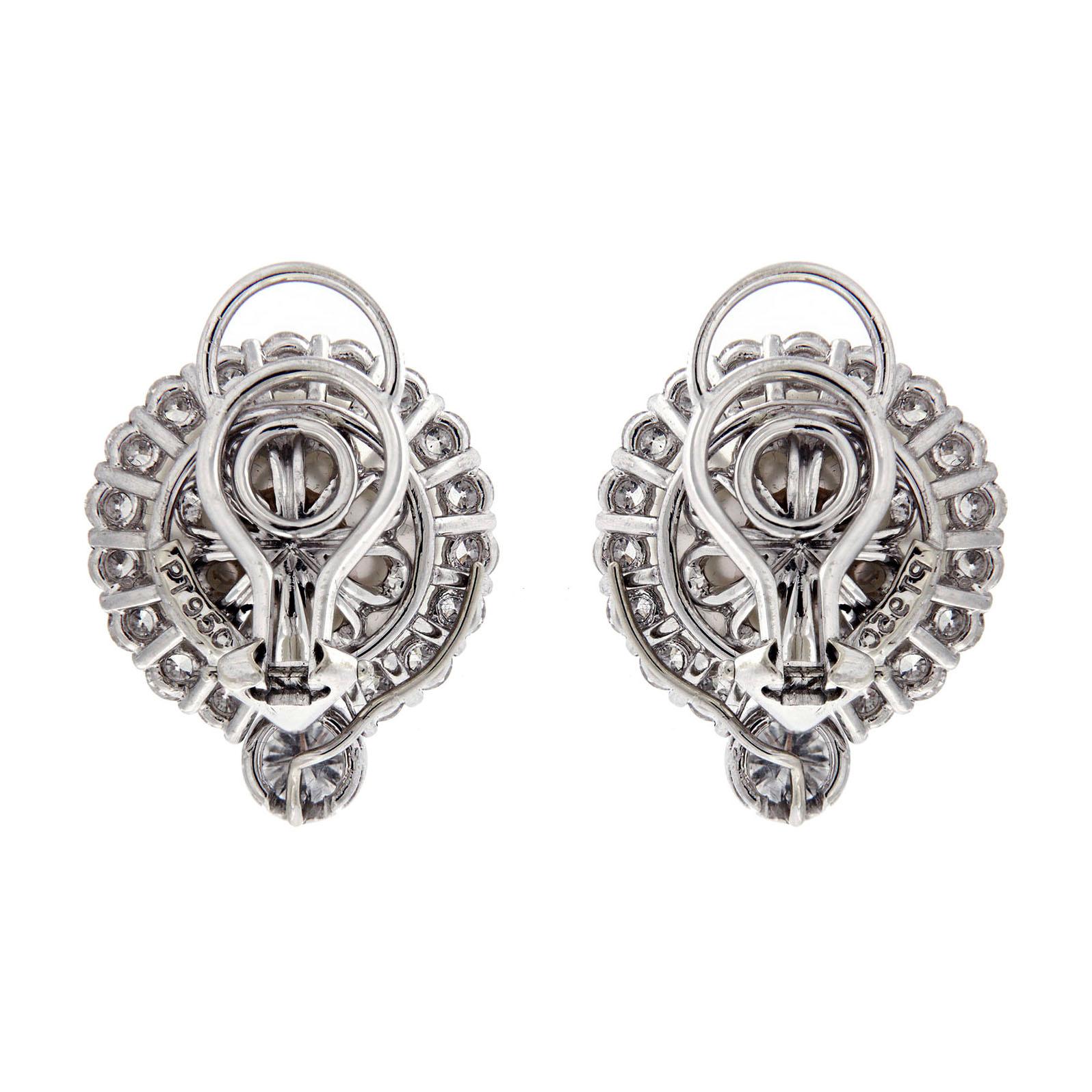 Diamonds add brilliance to these earrings, while white South Sea pearls serve as the focus. A thin border of round brilliant cut diamonds set in platinum outline each pearl. Larger, bezel set diamonds sit beneath the pearls. There are 36 round