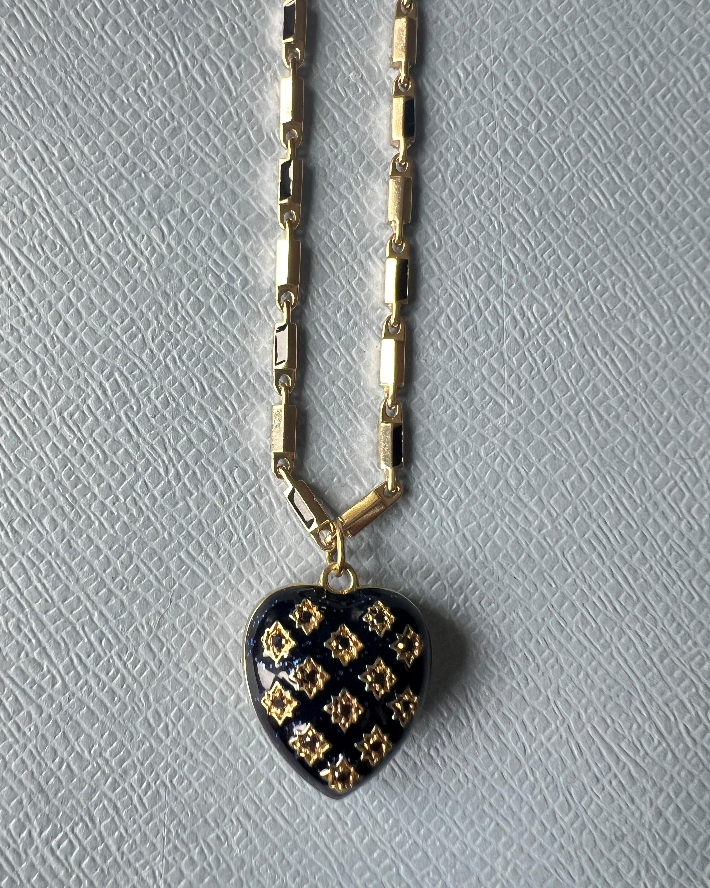 Questa collana simbolica di J DAUPHIN presenta un ciondolo a forma di cuore realizzato in ottone placcato oro, riccamente rivestito di smalto glitterato blu notte e con diamanti neri naturali incastonati. La forma a cuore gonfia e dimensionale