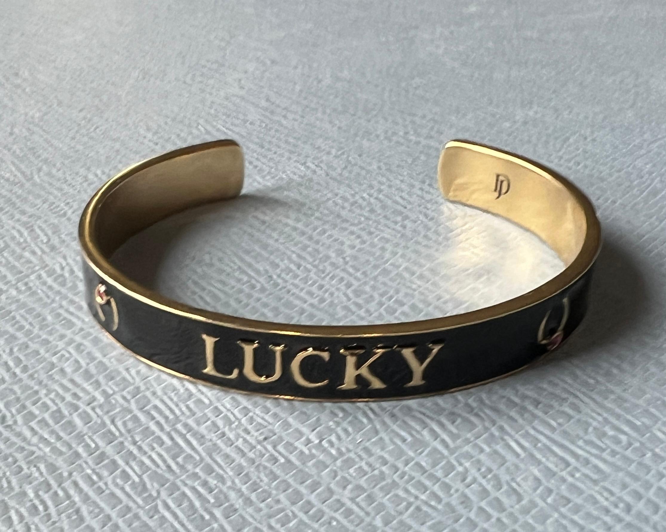 LUCKY Horseshoe Cuff Bracelet in Gold-Plated Brass with Black Enamel and Ruby – Symbolic Jewelry by J Dauphin
This powerful cuff bracelet by designer J Dauphin features the word “LUCKY” in bold black enamel across a sculptural 14k gold-plated brass
