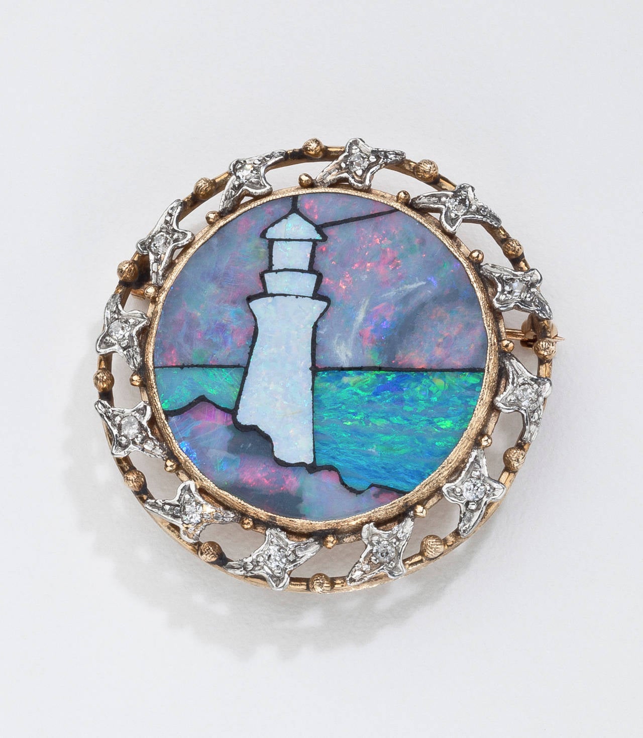 An antique inlaid opal brooch of a lighthouse.  The charming scene of a lighthouse on a rock outcrop overlooking the ocean is highlighted with varying types of inlaid opal, surrounded by 12 old European  and old miner's cut diamonds and set in 14