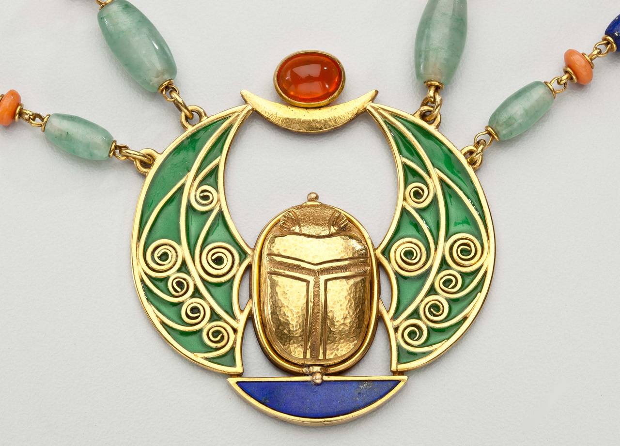 A rare and elegant scarab  necklace by Marcus &  Co.  The 18 karat gold and gem stone necklace is highlighted by a plique a jour pendant that features a large gold scarab.  A swag chain surrounds the necklace and is interspersed by five gold scarabs