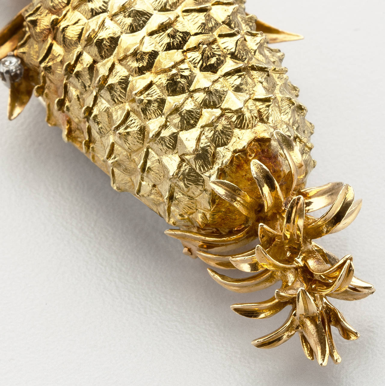 An 18 karat gold clip brooch by Tiffany of a pineapple with diamond accents.  The pineapple, which is textured to simulate the surface of the fruit, is highlighted by six full cut diamonds accenting the fruit's leaves.  Signed Tiffany & Co, France. 