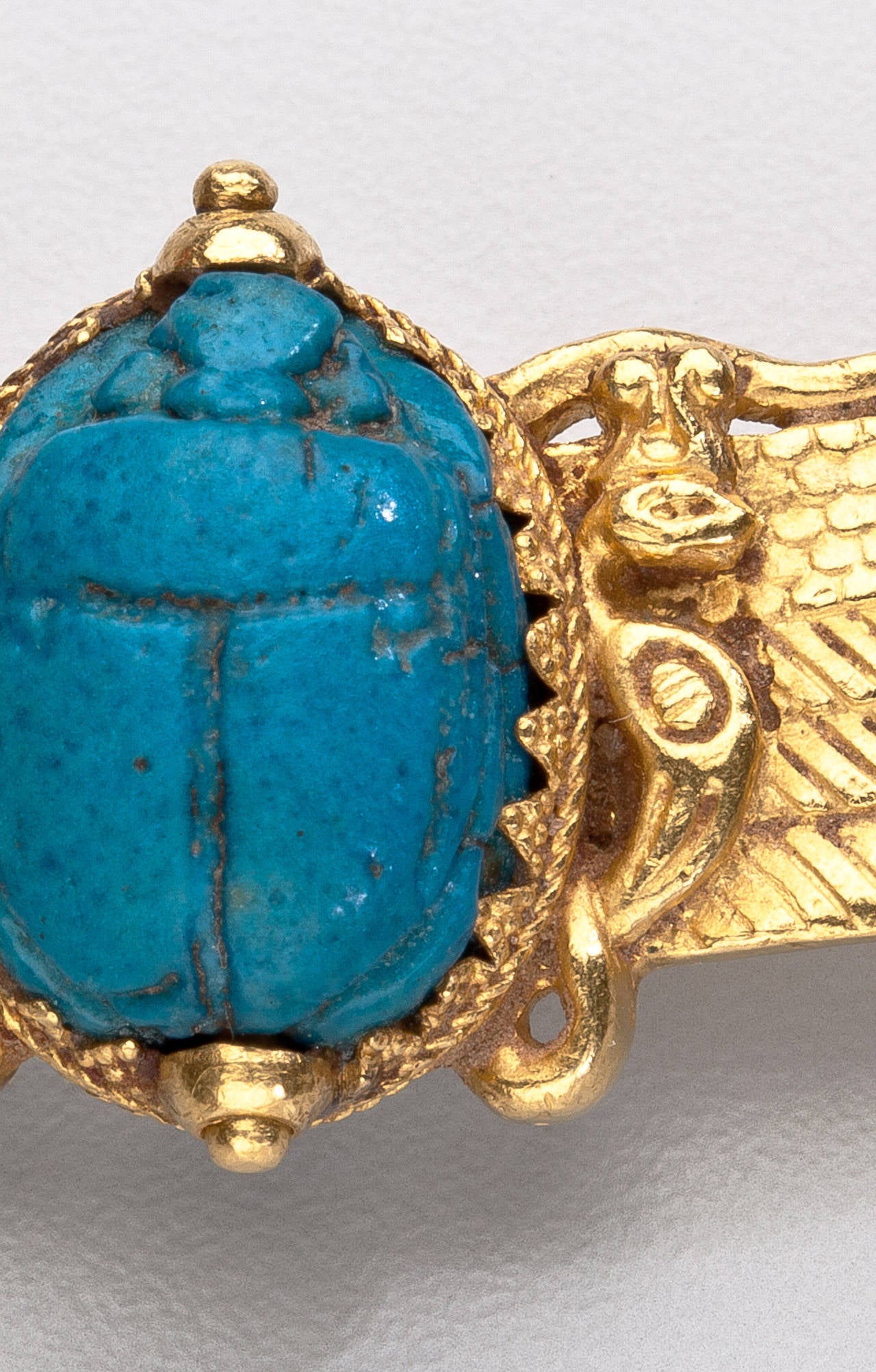 An antique scarab brooch in the Egyptian Revival style by Jules Wiese.  The high karat gold brooch has chased wings with two vultures supporting a turquoise hardstone scarab.  Gold granulation surrounds the bezel prongs supporting the scarab.  The