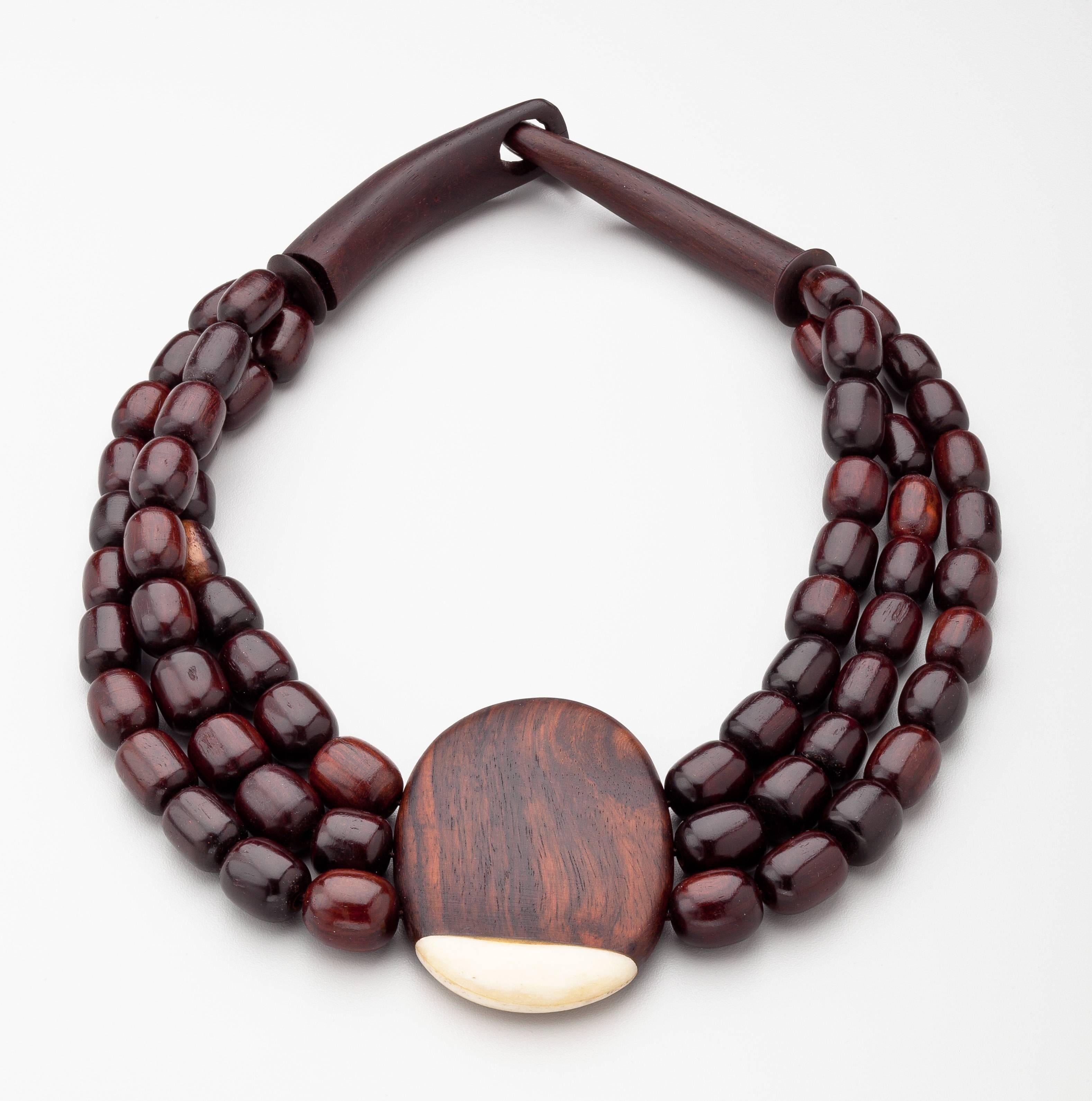 A triple strand ebony necklace by Catherine Noll (1945 - 1992)  the French designer of haute couture jewelry.  The lozenge shaped wood beads suspend a disc of wood with a small highlight of ivory.  This necklace has the iconic Catherine Noll hook