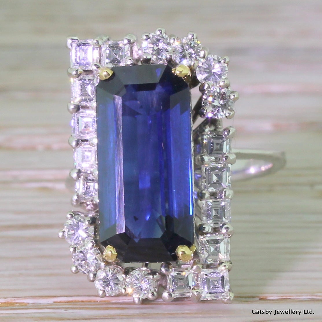 An astonishing sapphire - natural and with no enhancements - set in a quite astonishing ring. The 5.96 carat sapphire is a perfect glowing cornflower blue. Eight brilliant round cut diamonds and twelve square cuts surround the sapphire. The square