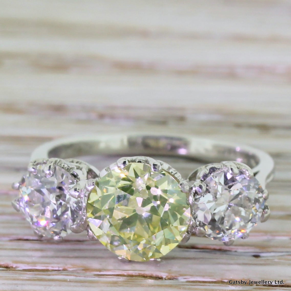 Throw any superlative at this ring, and it will stick. An impossibly rare greenish yellow old cut diamond - weighing just under 2.00 carat - flanked by a pair of colourless white diamonds. For a ring with so much diamond weight, this is a very easy