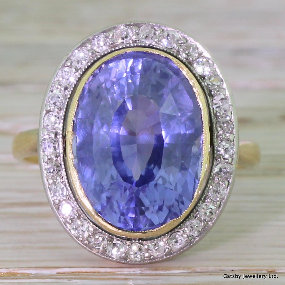 An immense natural and unenhanced sapphire showcased in a stunning ring. The sky blue sapphire holds distict flashes of purple and is a very clean and clear. Rubover set in yellow gold with a floating halo of diamonds encircling it. The 28 old cut