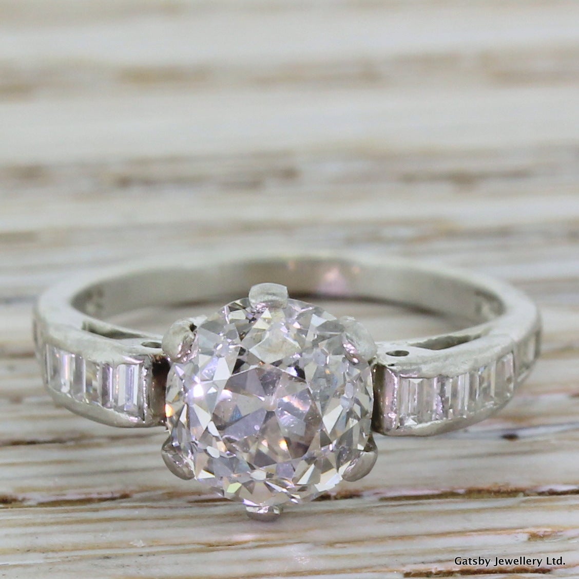 Yes, please! There is so much to love about this. The very clean old mine cut diamond in the centre bursts with life and fire, and is set in one of the beautiful mounts we've ever had. Scrolled shoulders set with high white baguette cuts, with