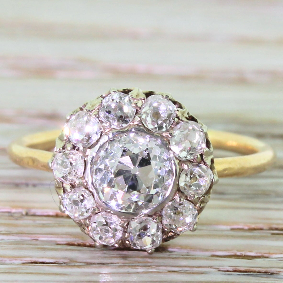 A bright white and clean old mine cut diamond, rubover set with 10 smaller old cut diamonds in the surround. The claw-set smaller diamonds lead to a pierced gallery and a very fine, simple gold band. Although this sits nice and close to the finger,