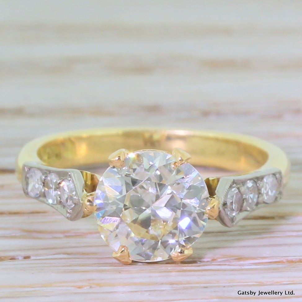 Bright, big and beautiful. The absolutely arresting old European cut diamond is a very light yellow and veritably busting with vibrancy and fire. Mounted in a six claw collet with an open gallery. The shoulders of the ring are adorned with