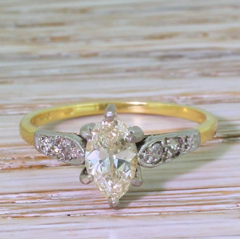 A wonderfully quirky diamond engagement ring. The old marquise cut diamond is internally clean, displays plenty of fine with a warm, soft champagne hue. The centre is secured in a six claw platinum collet, with diamond set spear-shaped shoulders to