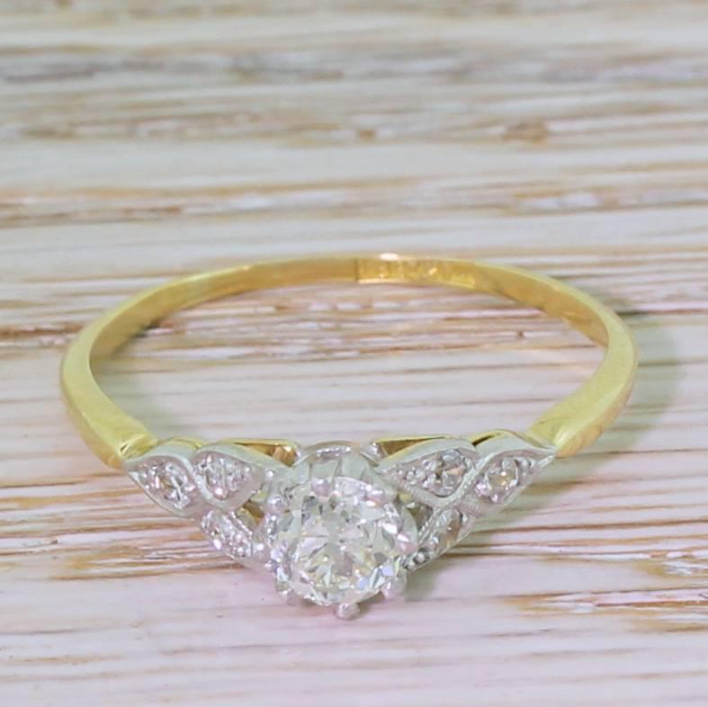 An exceedingly beautiful diamond engagement ring. The centre stone – coming in at just over half a carat – is secured in an eight claw coronet collet, and is framed stylised trefoil platinum shoulders to a slim, 18k yellow gold shank. An absolute