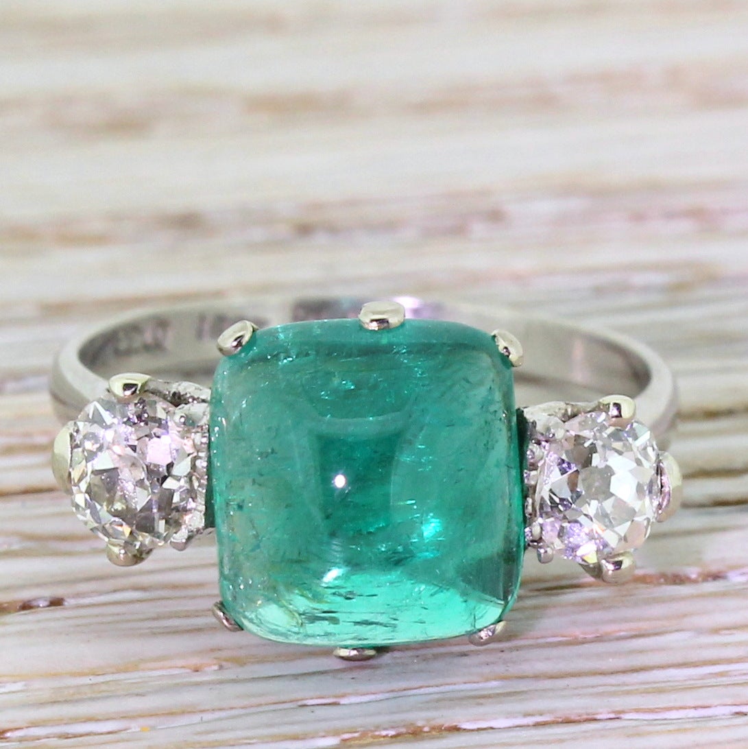 Simply sublime. A trilogy centred by one of finest emeralds you’re likely to find in a ring. Polished to a cabochon in an unusual “soft pyramid” shape, and flanked by a couple of sizeable old mine cut diamonds, both of a very high colour and