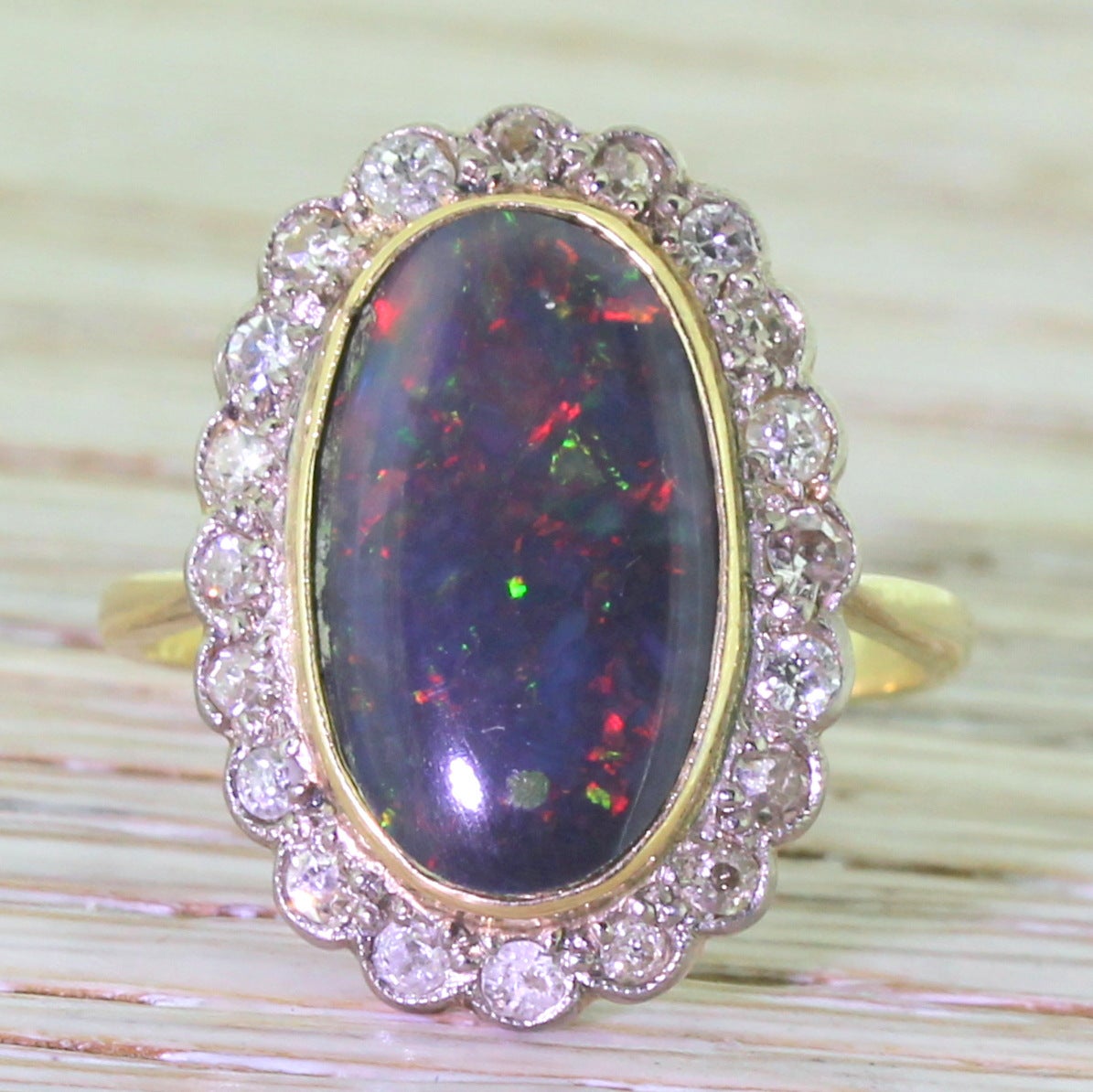 This wonderful and dramatic black opal show an impressive play of colours. Rubover set in yellow gold, the opal is surrounded by 20 old cut diamonds in platinum. The beautiful pierced gallery leads to a simple D-shaped yellow gold band. Sits nice