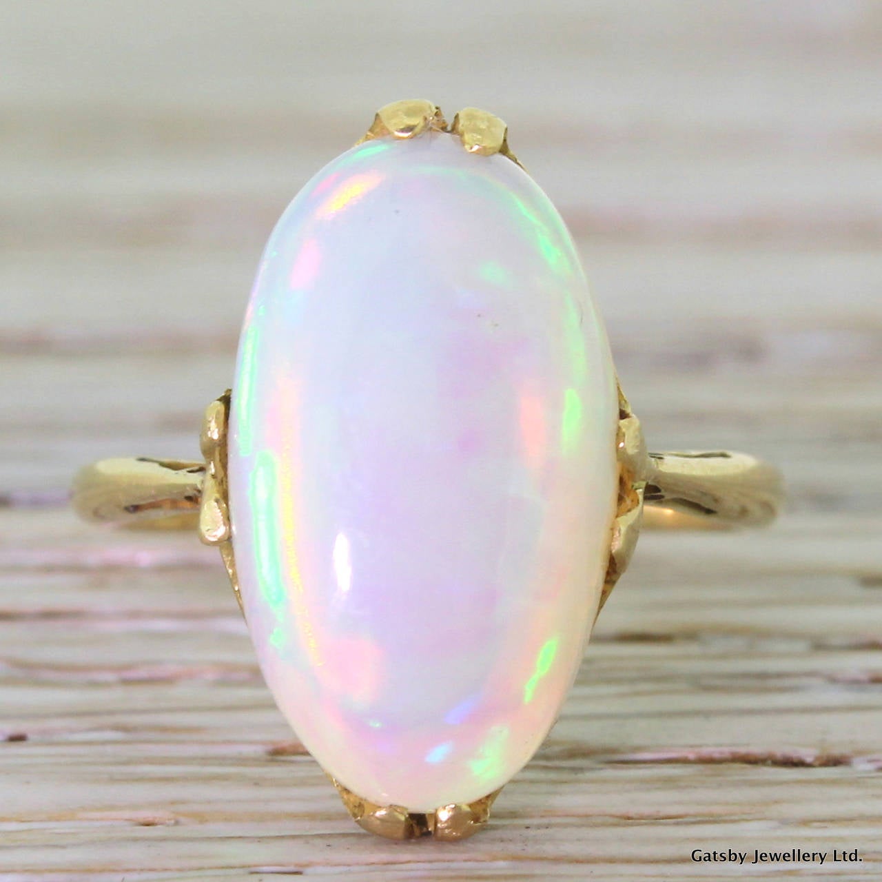 An electric opal mounted in a fine and delicate setting. The opal displays a very impressive play of colour, with bright flashes of neon green and orangey red. Secured by four double claws leading to a graceful open gallery.