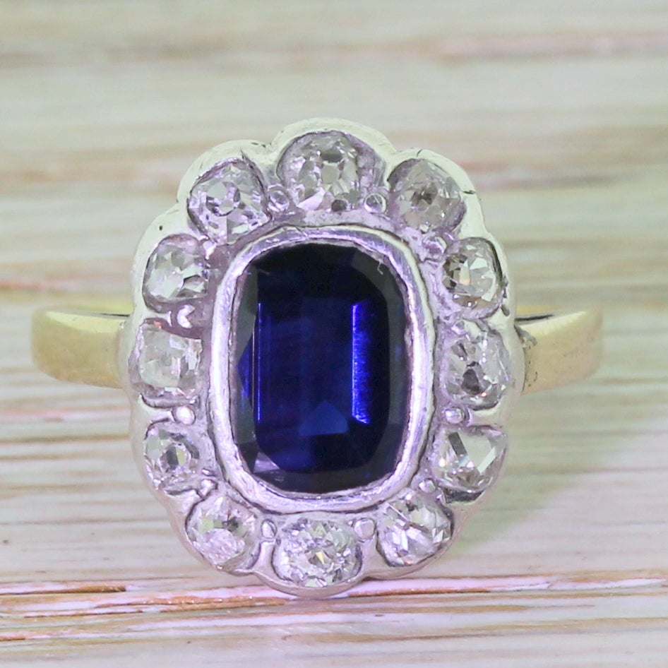 A fine mid-Victorian cluster ring, set with a deep royal blue sapphire. Rubover set in silver, the colour of the sapphire is highlighted by the colourless of the twelve old cut diamonds in the surround. A classic design, beautifully realised.

Cut
